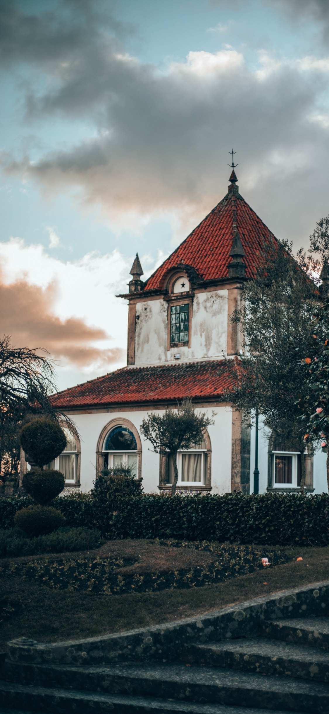 Red and White Concrete Building Near Green Trees Under White Clouds During Daytime. Wallpaper in 1125x2436 Resolution