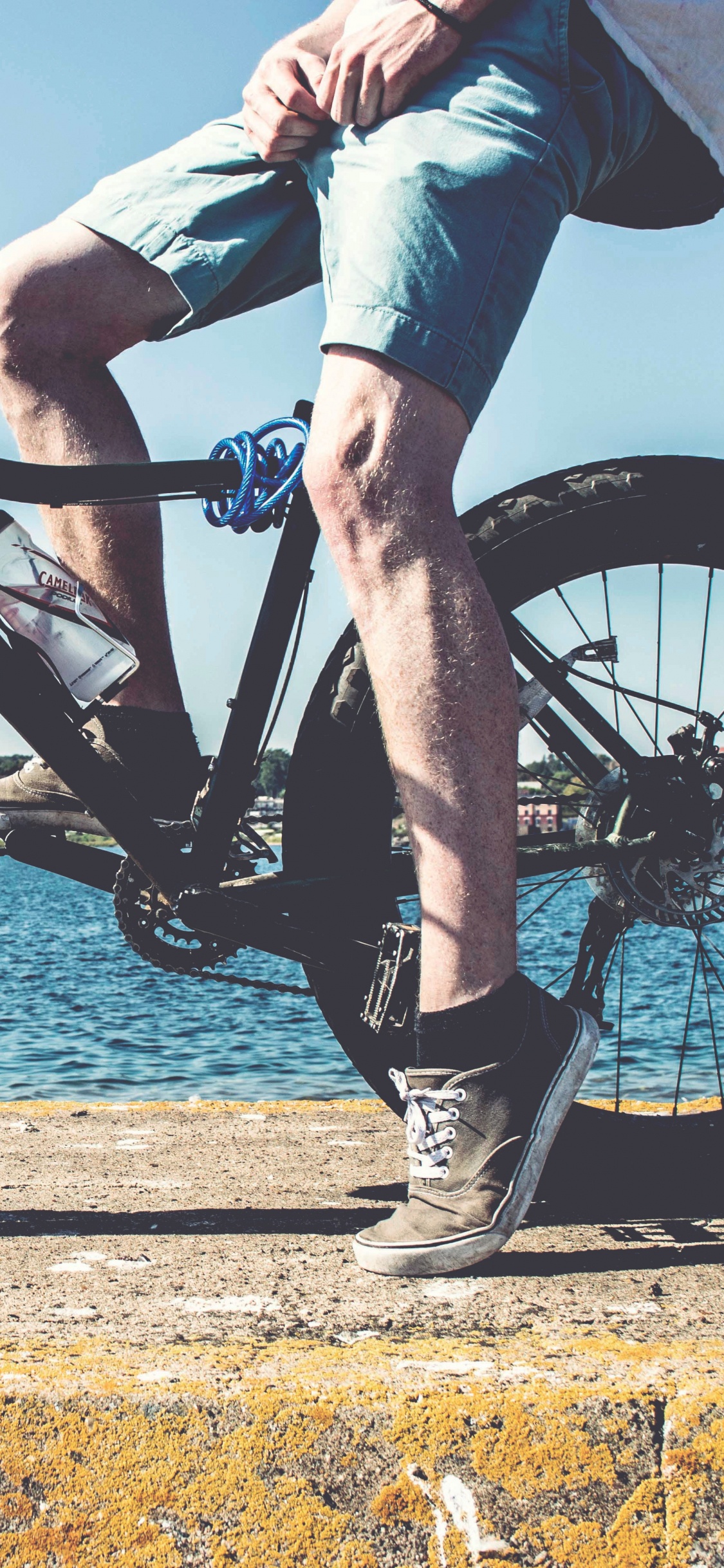 Persona en Blue Jeans Montando Bicicleta de Montaña Negra Cerca Del Cuerpo de Agua Durante el Día. Wallpaper in 1125x2436 Resolution
