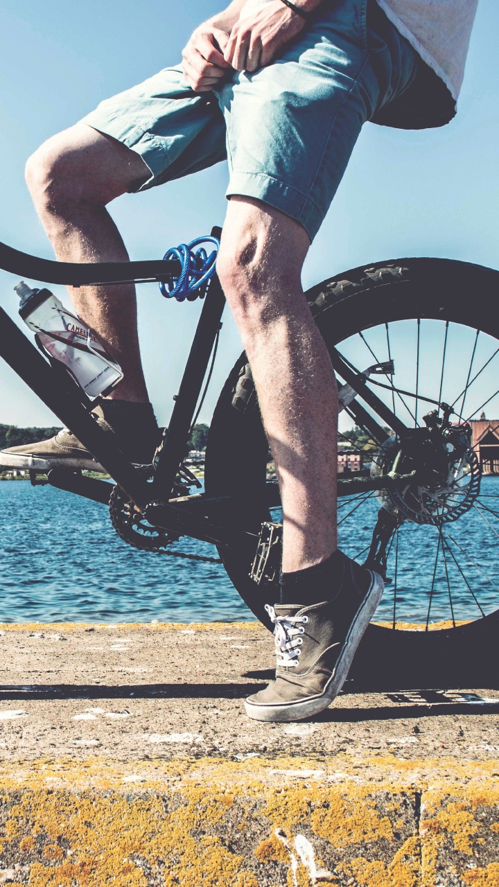 Person in Blue Denim Jeans Riding Black Mountain Bike Near Body of Water During Daytime. Wallpaper in 720x1280 Resolution