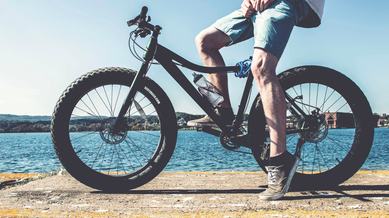Personne en Jeans Bleus Faisant du Vélo de Montagne Noir Près D'un Plan D'eau Pendant la Journée. Wallpaper in 1366x768 Resolution