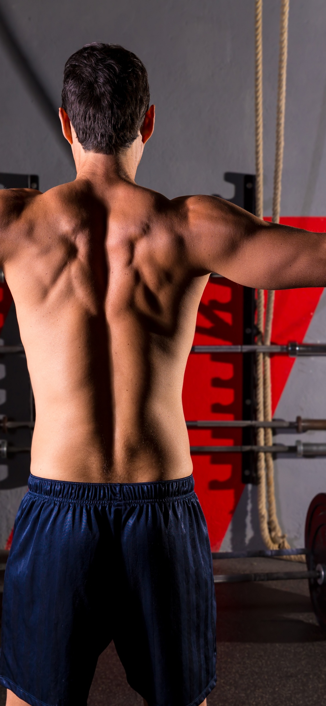 Mann in Blauen Shorts, Der in Der Nähe Von Schwarzen Und Roten Trainingsgeräten Steht. Wallpaper in 1125x2436 Resolution