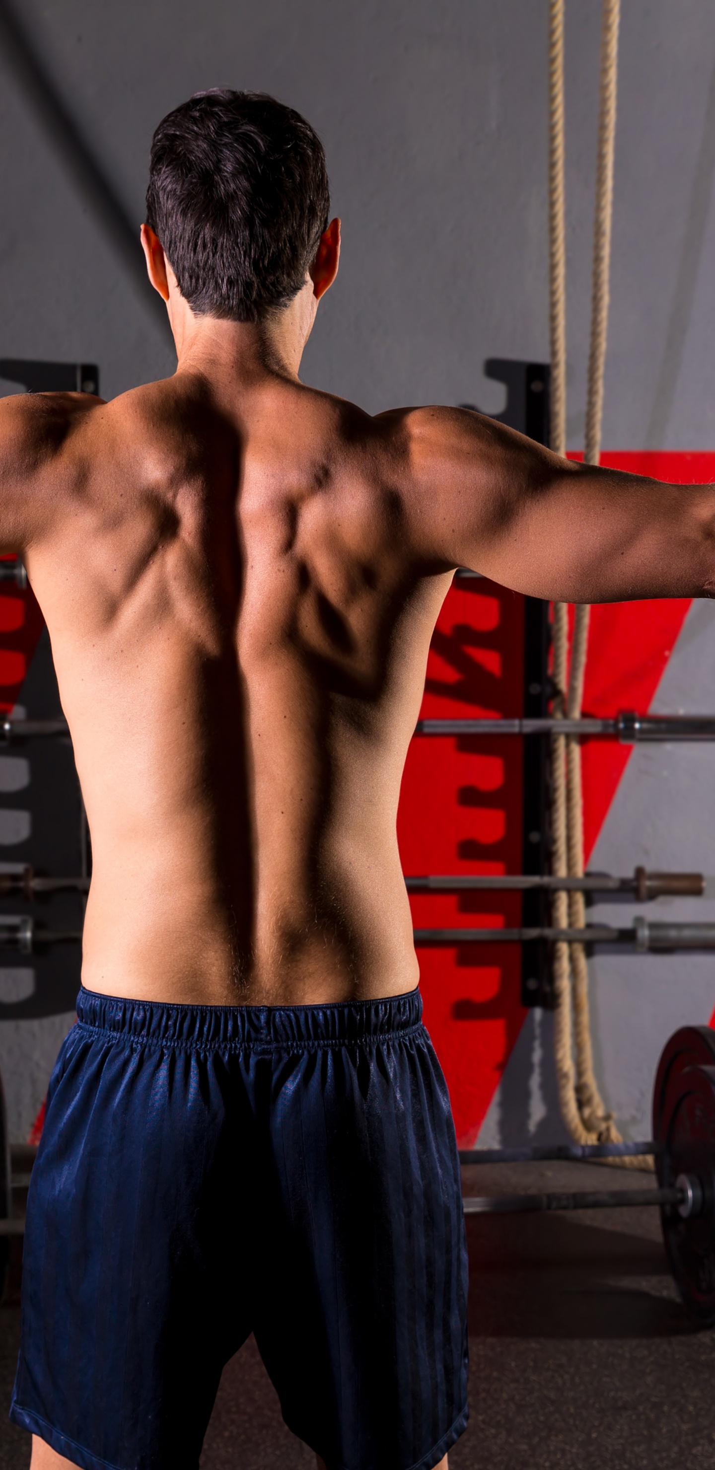 Man in Blue Shorts Standing Near Black and Red Exercise Equipment. Wallpaper in 1440x2960 Resolution