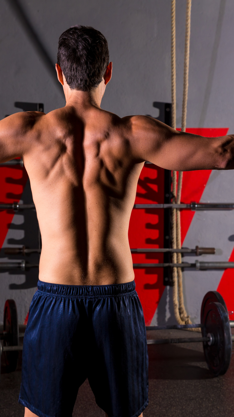 Man in Blue Shorts Standing Near Black and Red Exercise Equipment. Wallpaper in 750x1334 Resolution