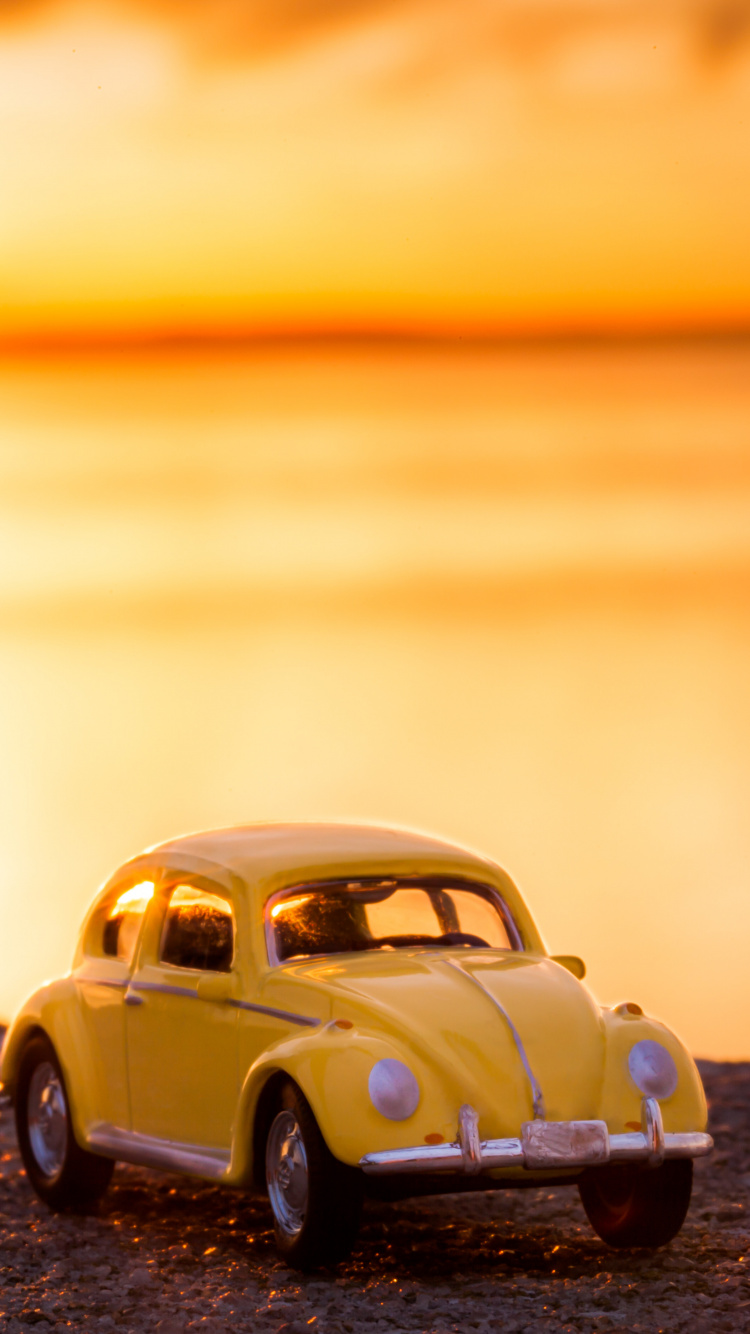 Gelber Volkswagen Käfer am Ufer Bei Sonnenuntergang. Wallpaper in 750x1334 Resolution