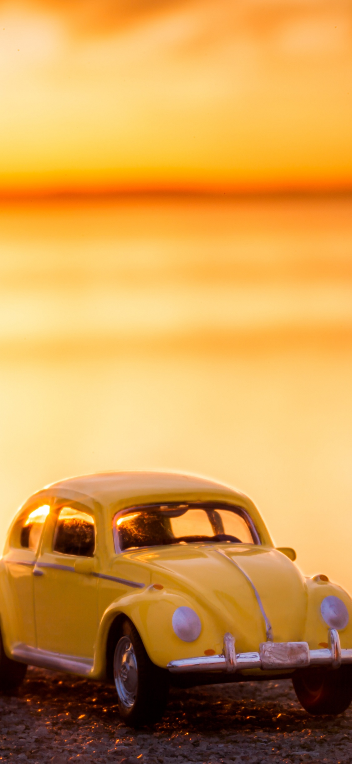 Volkswagen Beetle Amarillo en la Orilla Durante la Puesta de Sol. Wallpaper in 1125x2436 Resolution