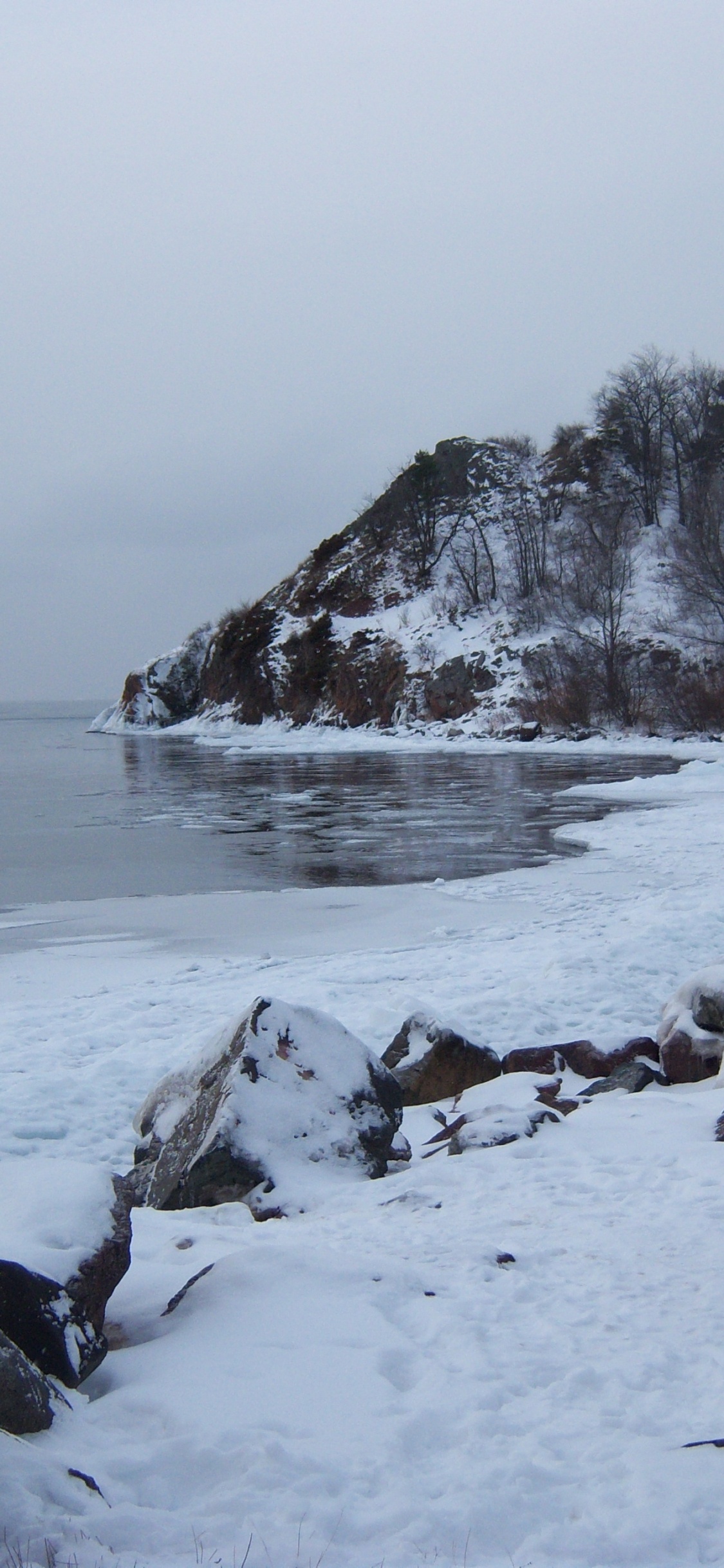 Snow Covered Rocks by The Sea During Daytime. Wallpaper in 1125x2436 Resolution