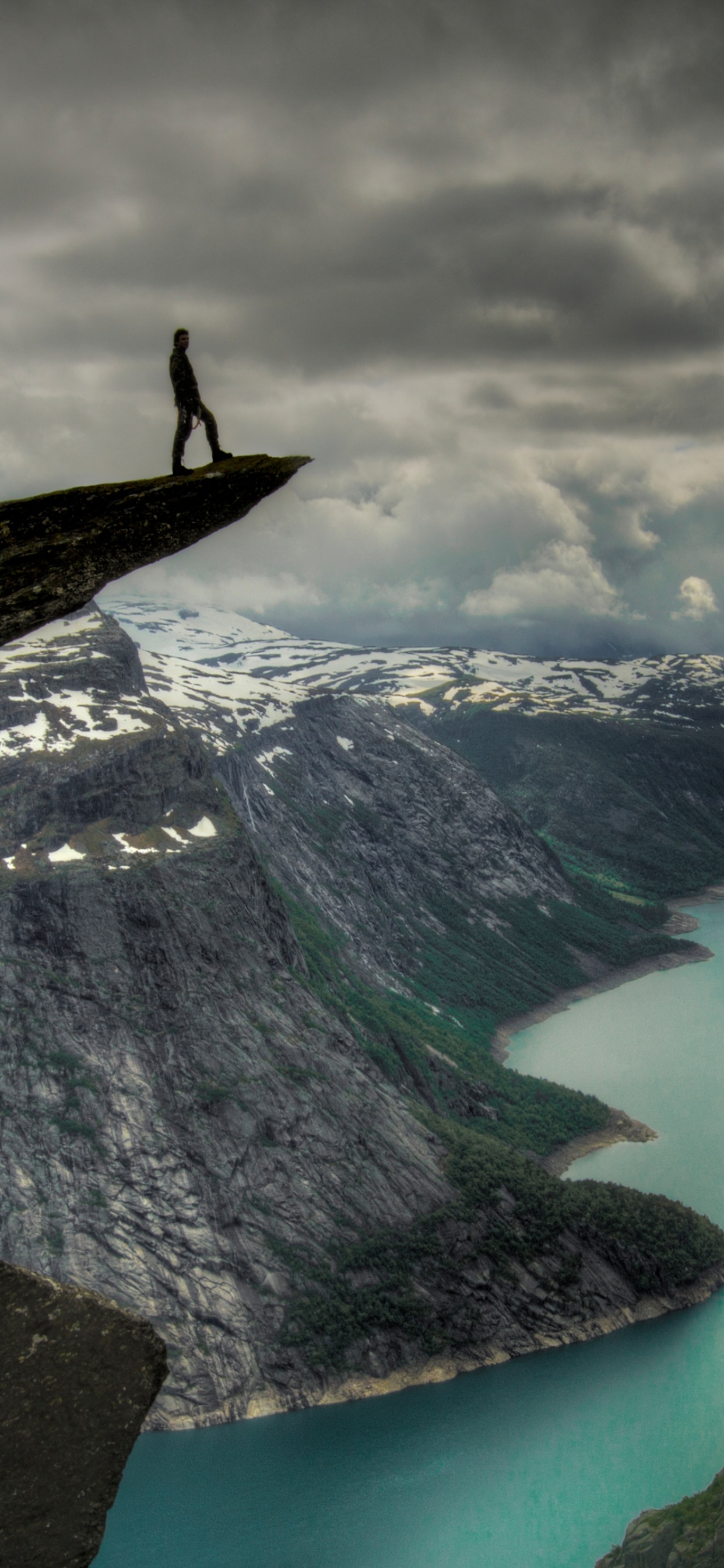 Person Standing on Rock Formation Near Lake Under Cloudy Sky During Daytime. Wallpaper in 1242x2688 Resolution