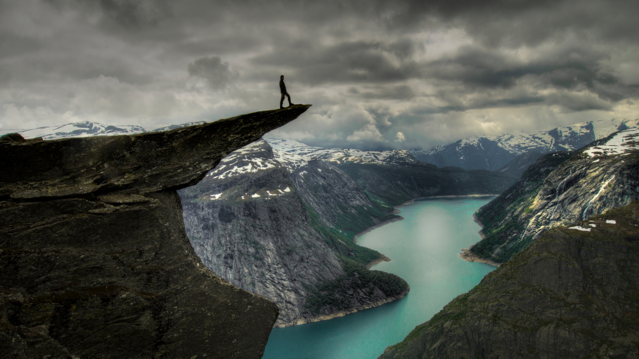 Person Standing on Rock Formation Near Lake Under Cloudy Sky During Daytime. Wallpaper in 1280x720 Resolution