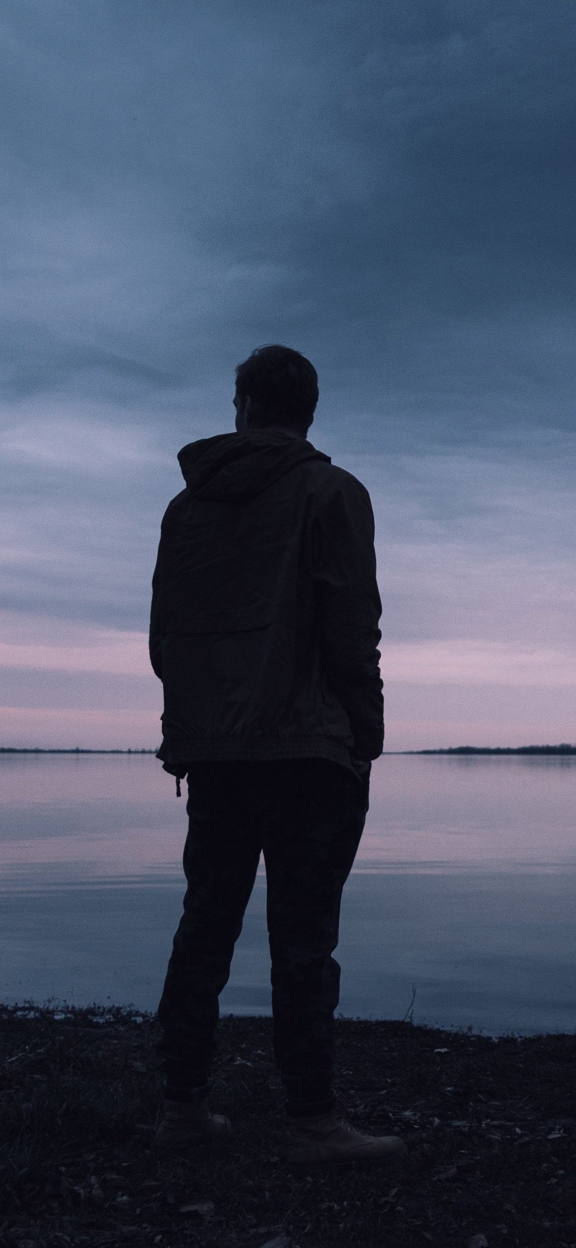 Man in Black Jacket Standing Near Body of Water During Daytime. Wallpaper in 1125x2436 Resolution