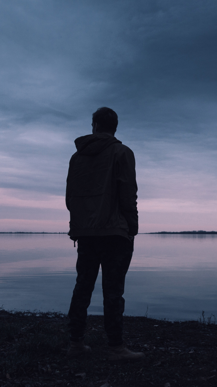 Man in Black Jacket Standing Near Body of Water During Daytime. Wallpaper in 750x1334 Resolution