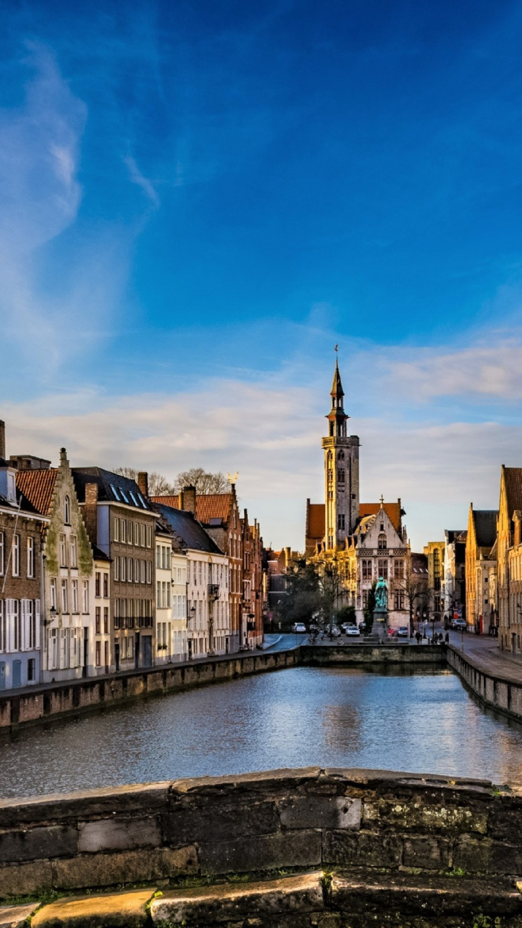 Brown and White Concrete Buildings Beside River Under Blue Sky During Daytime. Wallpaper in 750x1334 Resolution