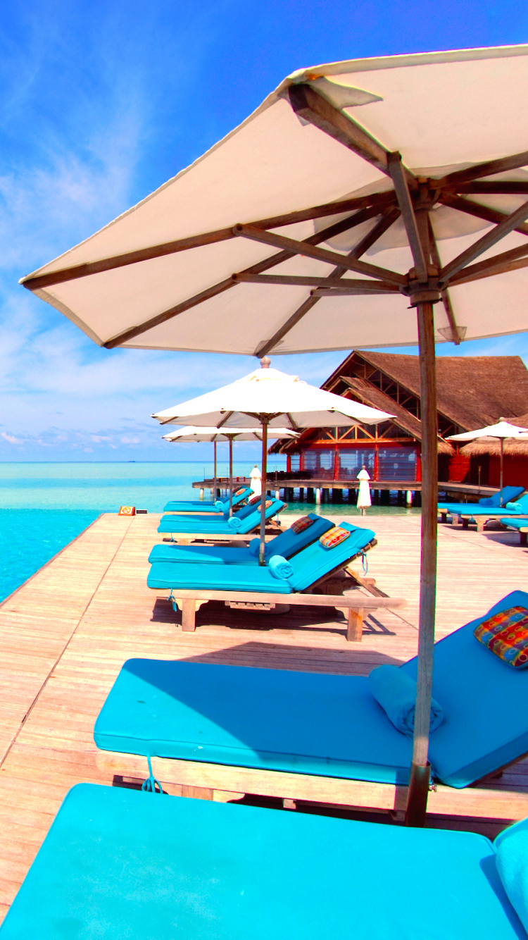 White and Brown Wooden Beach Lounge Chairs on Blue Sea Under Blue Sky During Daytime. Wallpaper in 750x1334 Resolution