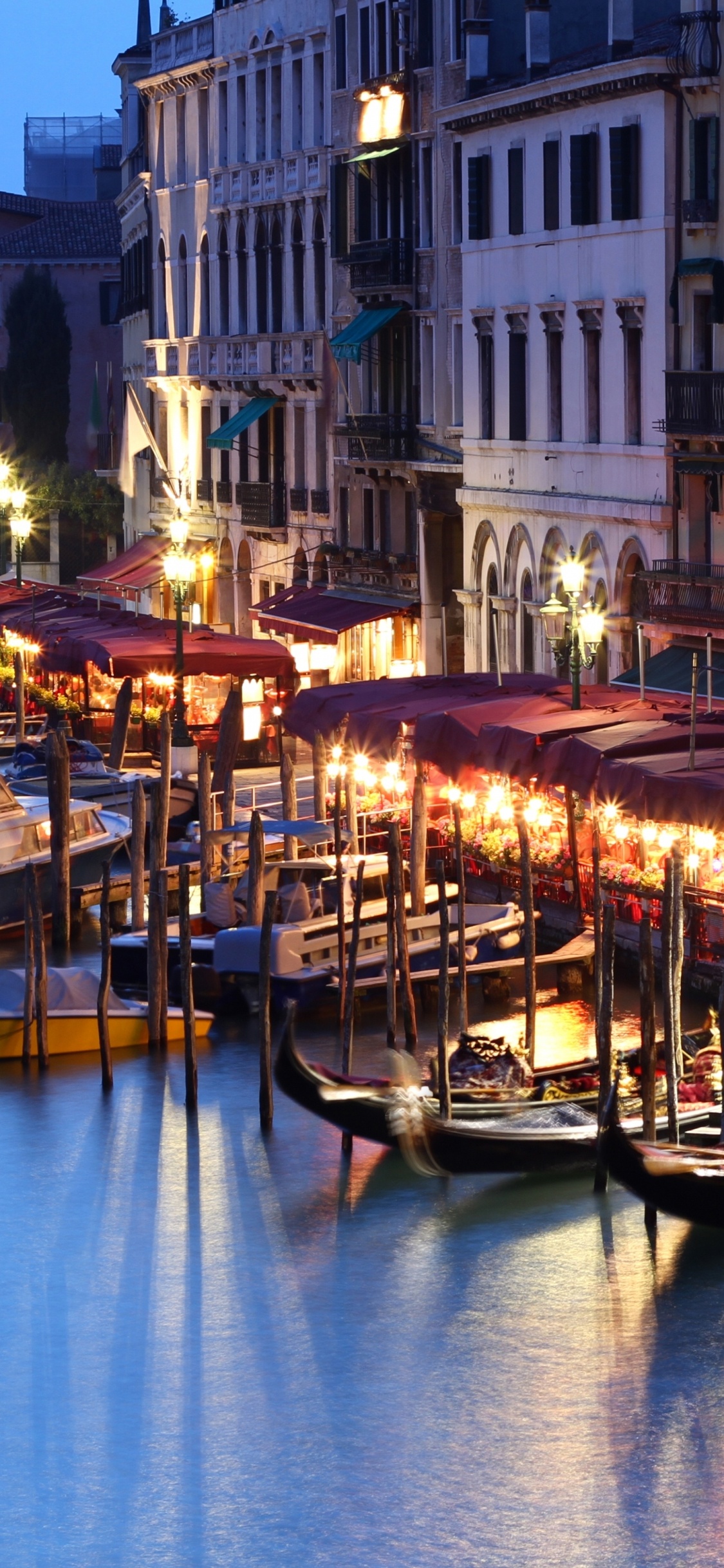 People Riding on Boat on River Near Buildings During Night Time. Wallpaper in 1125x2436 Resolution