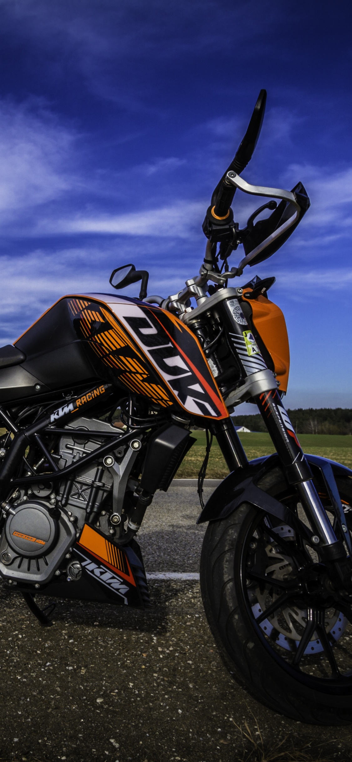 Orange Und Schwarzes Motorrad Auf Schwarzer Asphaltstraße Unter Grauem Bewölktem Himmel. Wallpaper in 1125x2436 Resolution