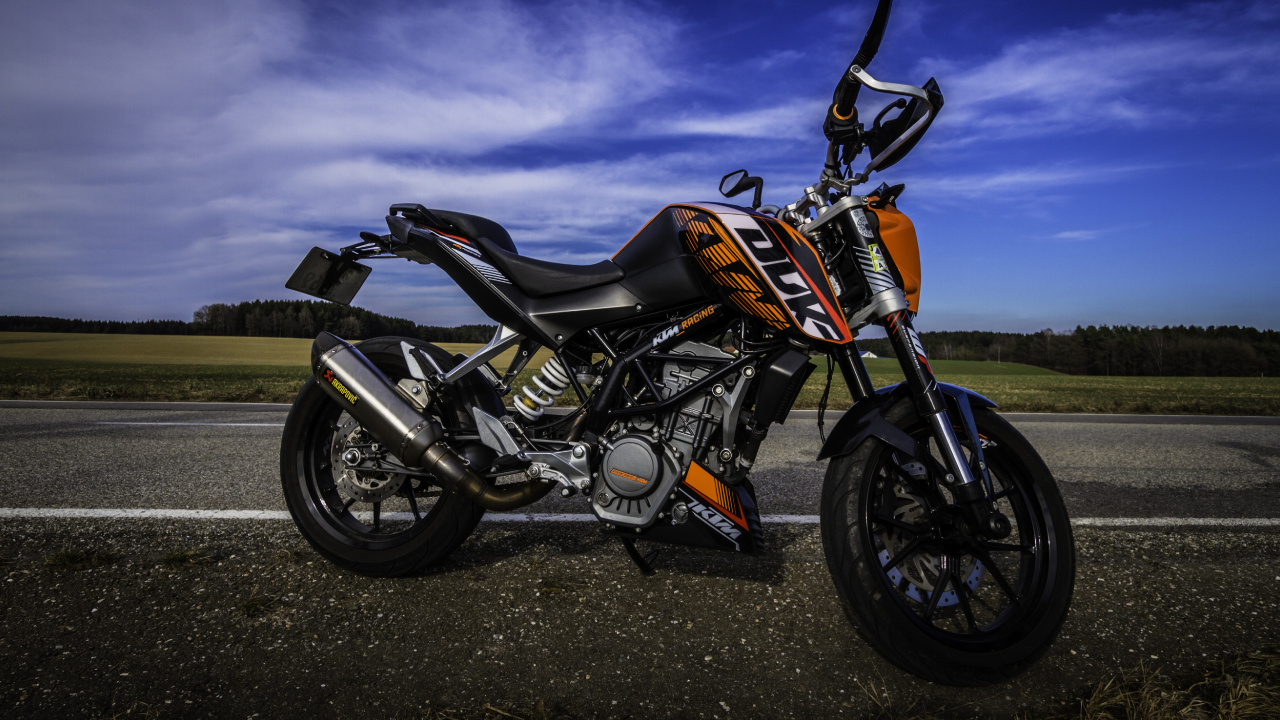 Orange and Black Motorcycle on Black Asphalt Road Under Gray Cloudy Sky. Wallpaper in 1280x720 Resolution