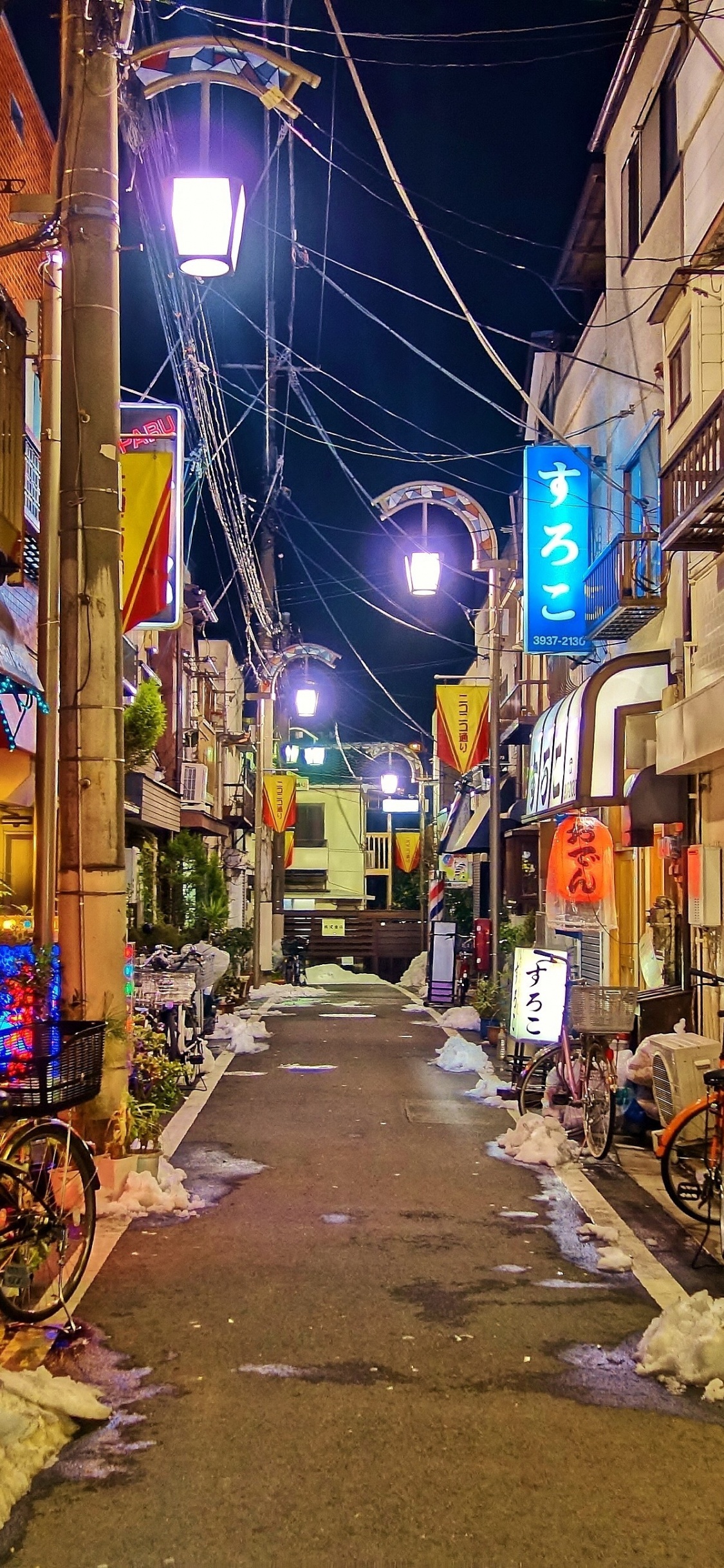 Empty Street With Cars Parked Beside Buildings During Night Time. Wallpaper in 1125x2436 Resolution