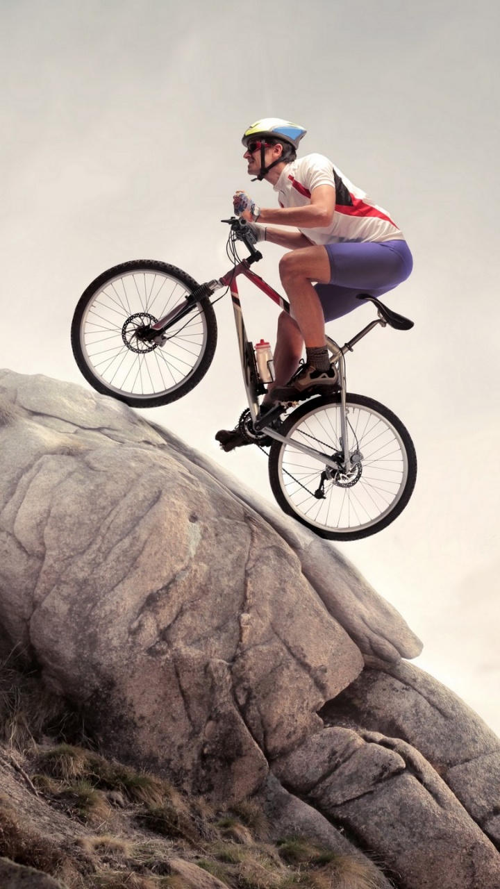 Mann in Weißem Hemd Und Schwarzen Shorts, Der Auf Einem Schwarzen Mountainbike Auf Einem Braunen Felsenberg Fährt. Wallpaper in 720x1280 Resolution