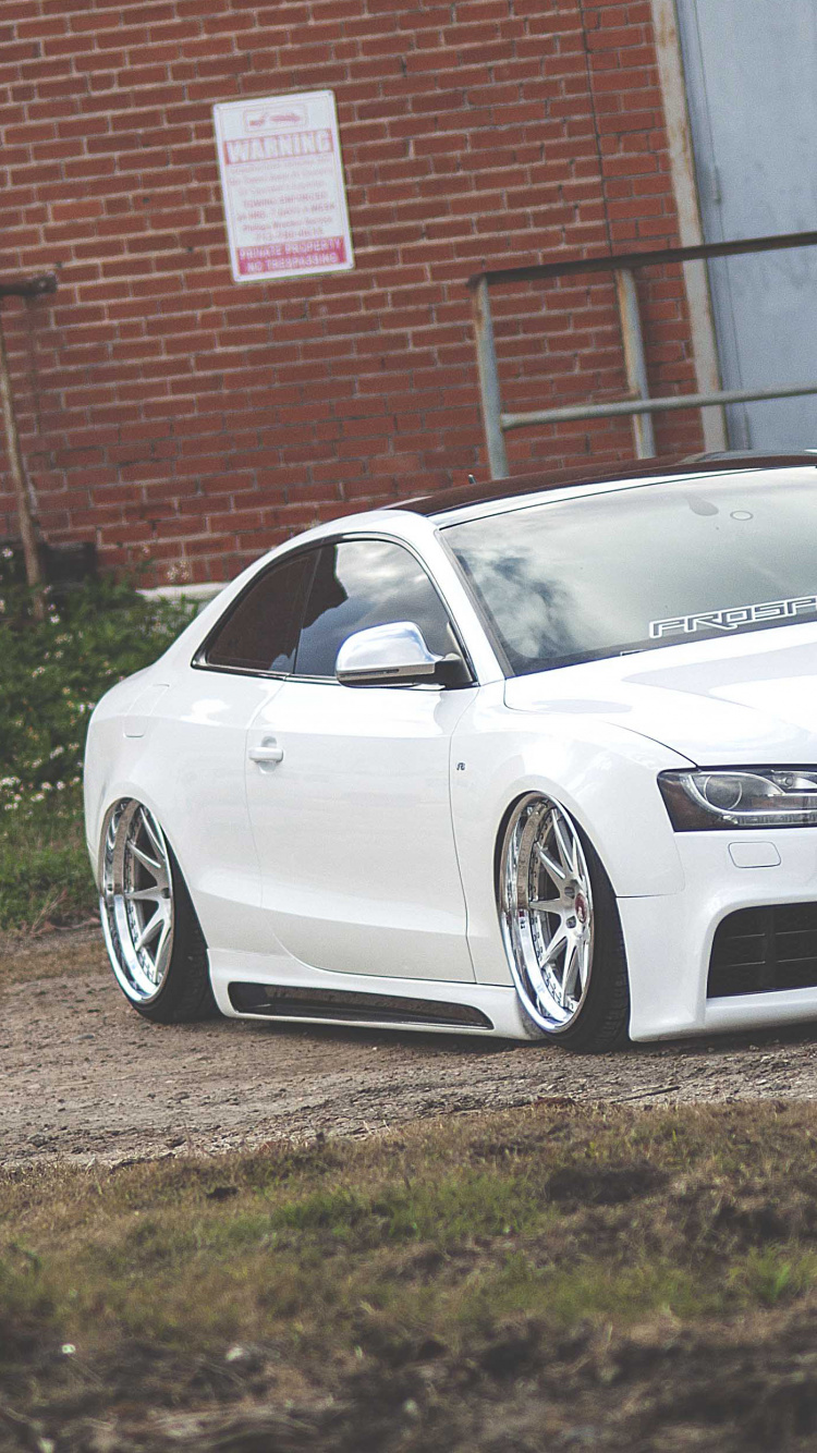 Audi r 8 Blanco Estacionado Cerca Del Edificio de Ladrillo Marrón. Wallpaper in 750x1334 Resolution