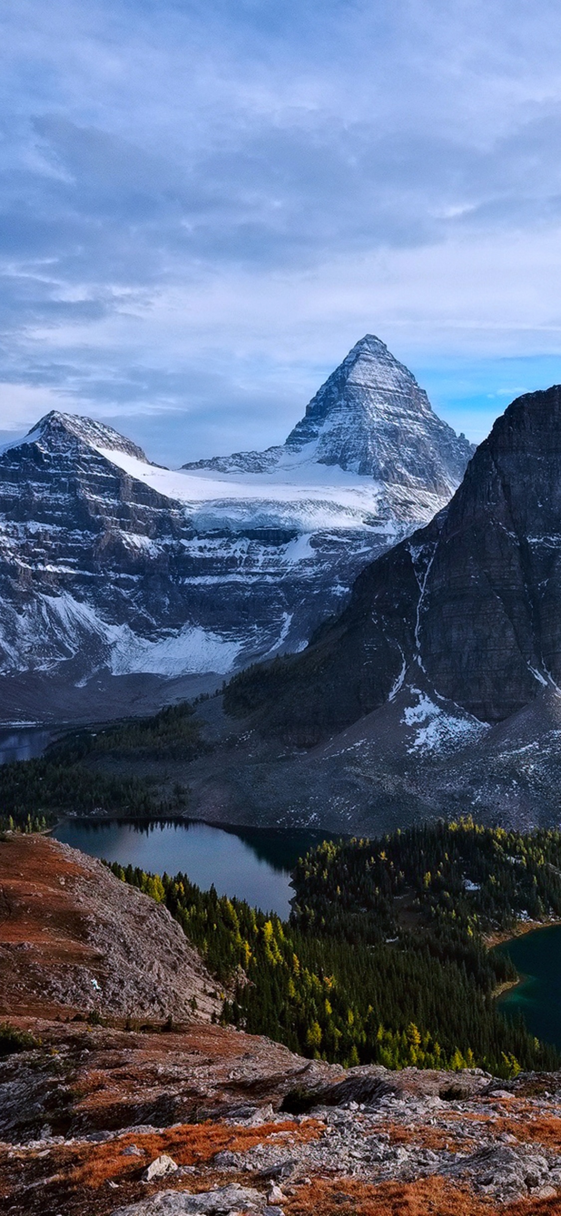 Snow Covered Mountain Near Lake Under Cloudy Sky During Daytime. Wallpaper in 1125x2436 Resolution