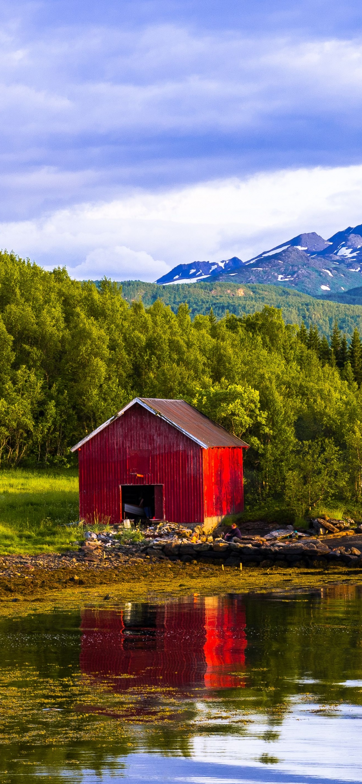 Braunes Holzhaus am See in Der Nähe Von Grünen Bäumen Und Bergen Unter Weißen Wolken Und Blauem Himmel. Wallpaper in 1242x2688 Resolution