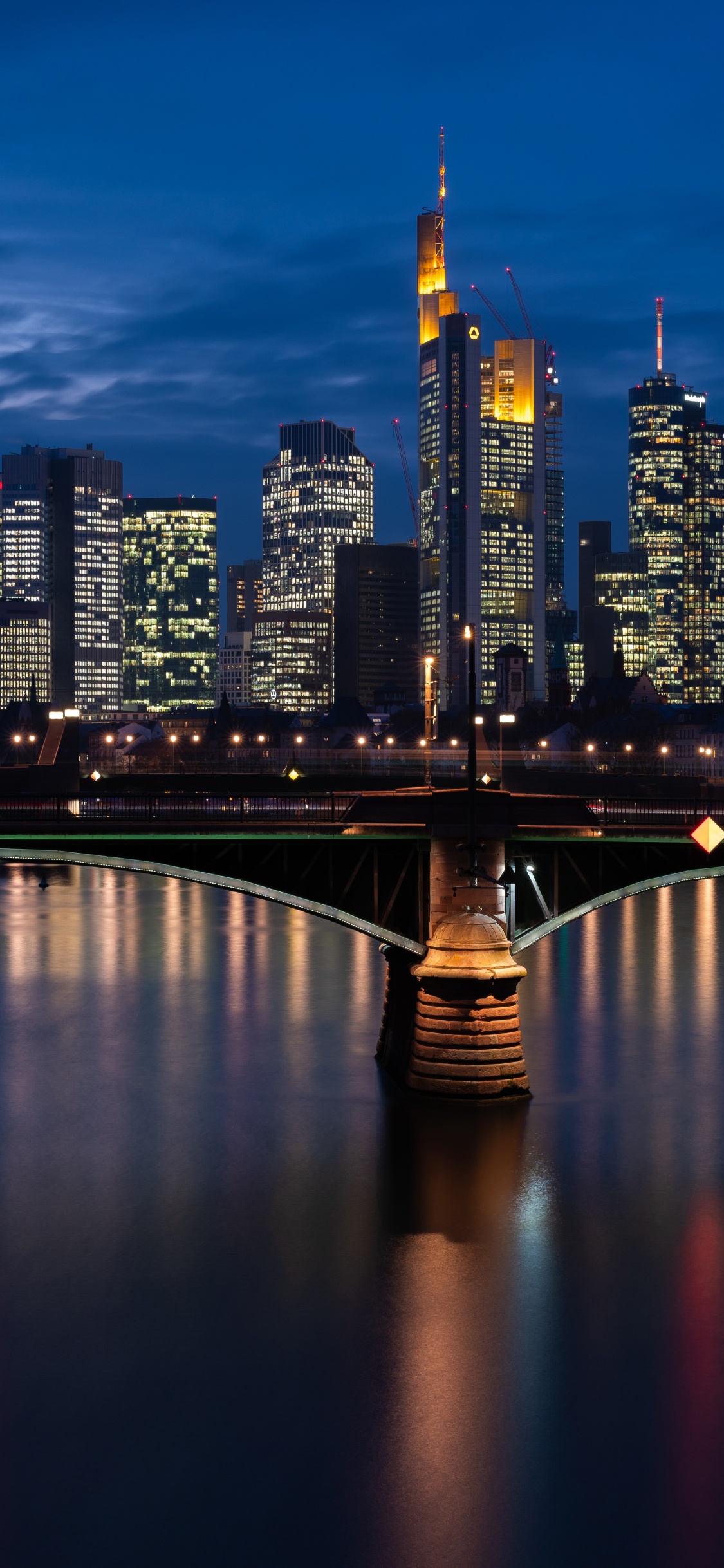 Puente Sobre el Río Cerca de Los Edificios de la Ciudad Durante la Noche. Wallpaper in 1125x2436 Resolution