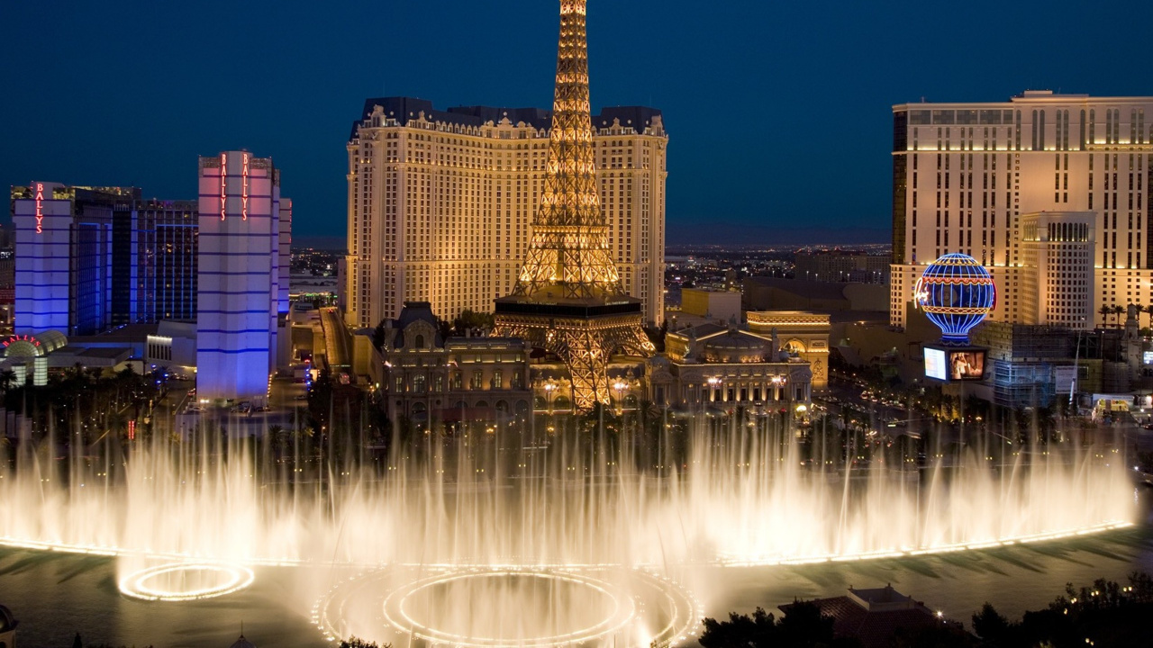 Water Fountain Near City Buildings During Night Time. Wallpaper in 1280x720 Resolution