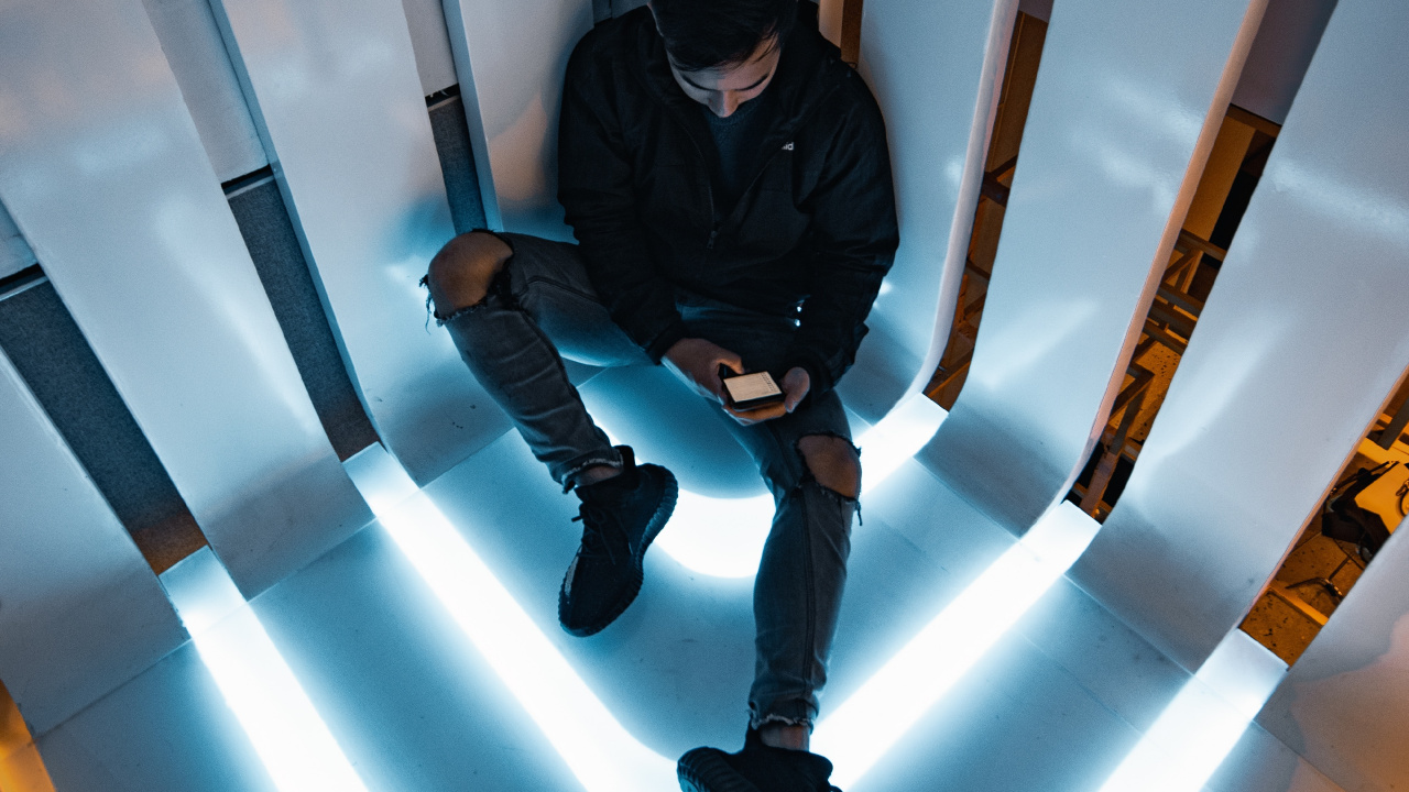 Man in Black Jacket and Black Pants Sitting on White Wall. Wallpaper in 1280x720 Resolution