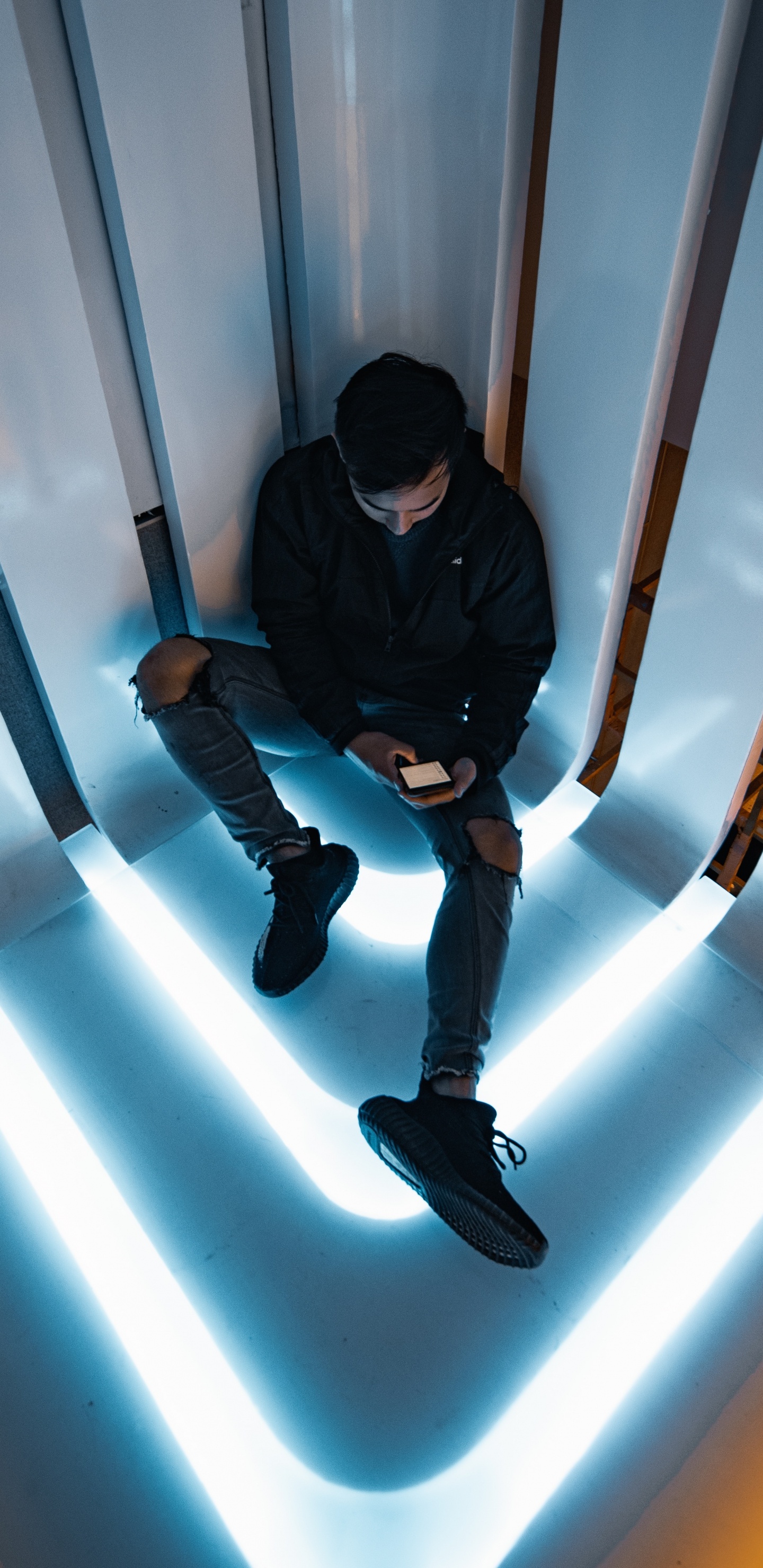 Man in Black Jacket and Black Pants Sitting on White Wall. Wallpaper in 1440x2960 Resolution