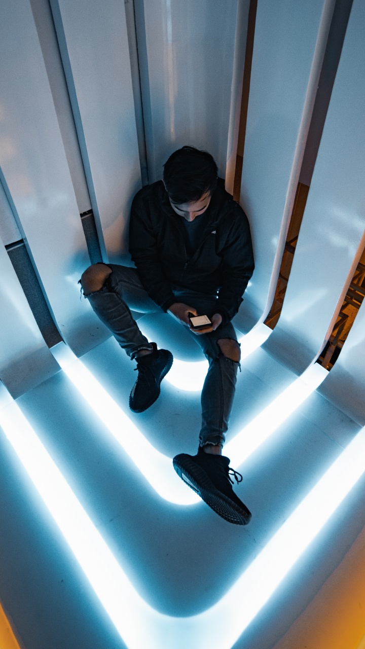 Man in Black Jacket and Black Pants Sitting on White Wall. Wallpaper in 720x1280 Resolution