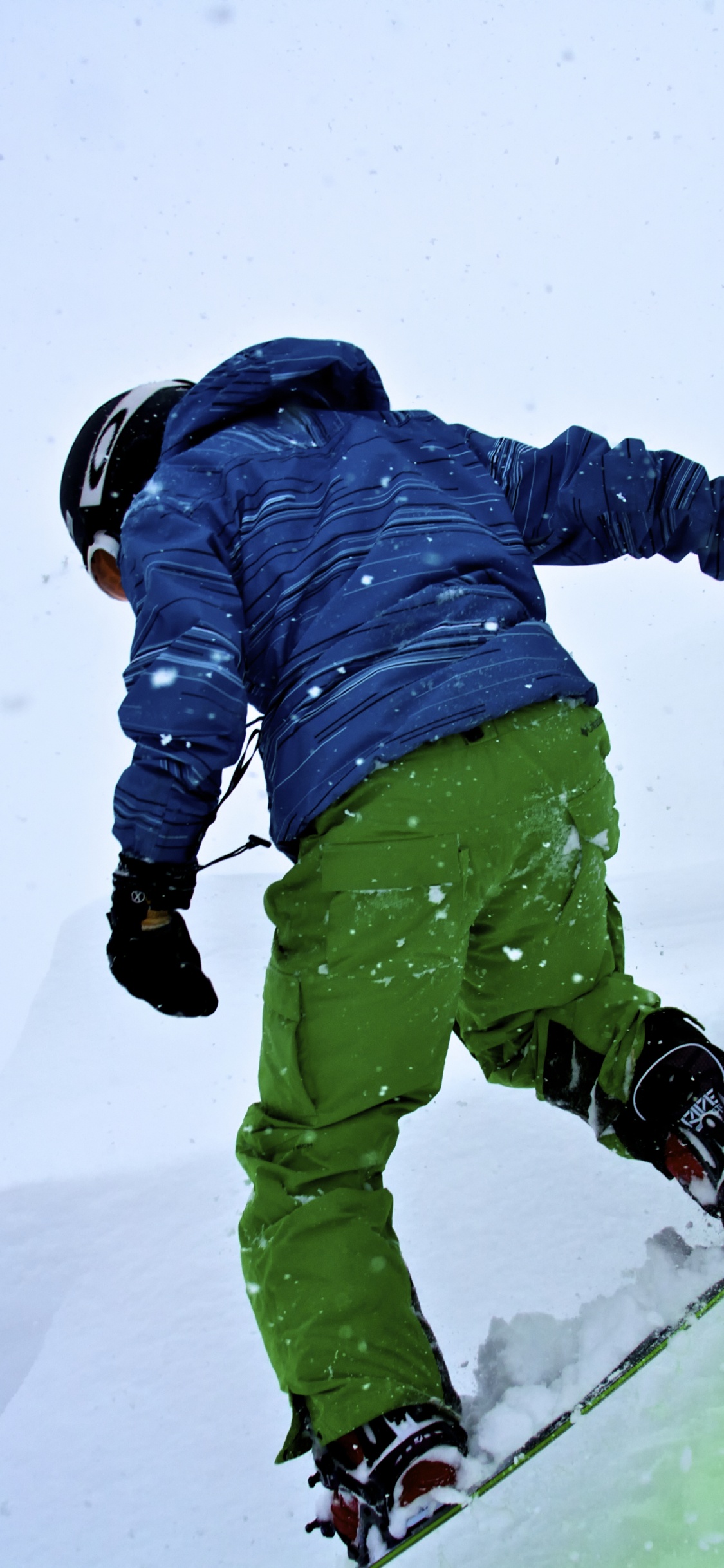 Persona Con Chaqueta Azul y Pantalones Verdes Montados Sobre Palas de Esquí Sobre un Terreno Cubierto. Wallpaper in 1125x2436 Resolution