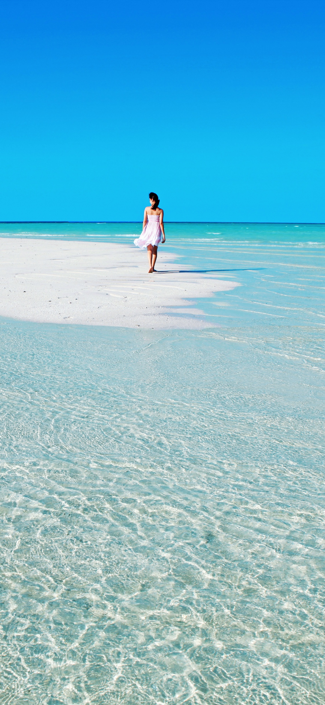 Mujer Con Camisa Blanca Caminando Por la Playa Durante el Día. Wallpaper in 1125x2436 Resolution