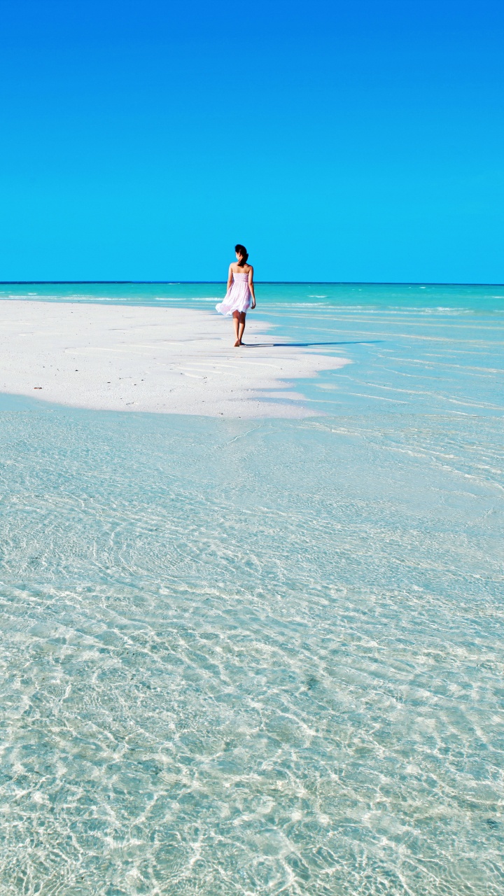 Mujer Con Camisa Blanca Caminando Por la Playa Durante el Día. Wallpaper in 720x1280 Resolution