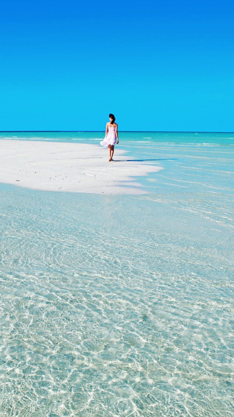 Mujer Con Camisa Blanca Caminando Por la Playa Durante el Día. Wallpaper in 750x1334 Resolution