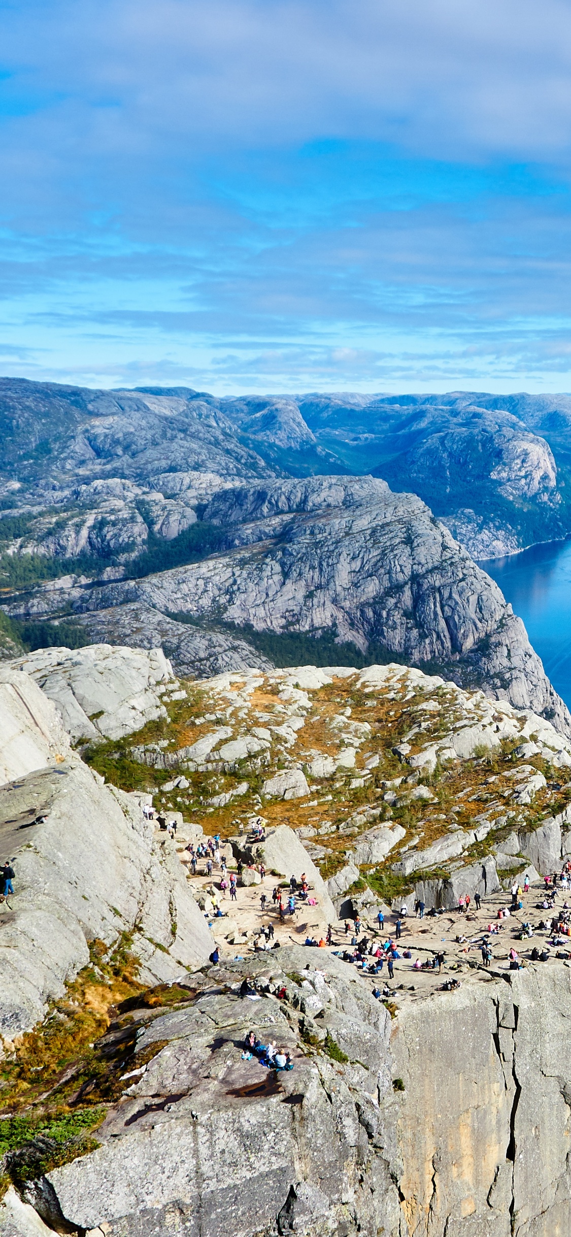 Blue Lake Between Gray Rocky Mountains Under Blue and White Sunny Cloudy Sky During Daytime. Wallpaper in 1125x2436 Resolution