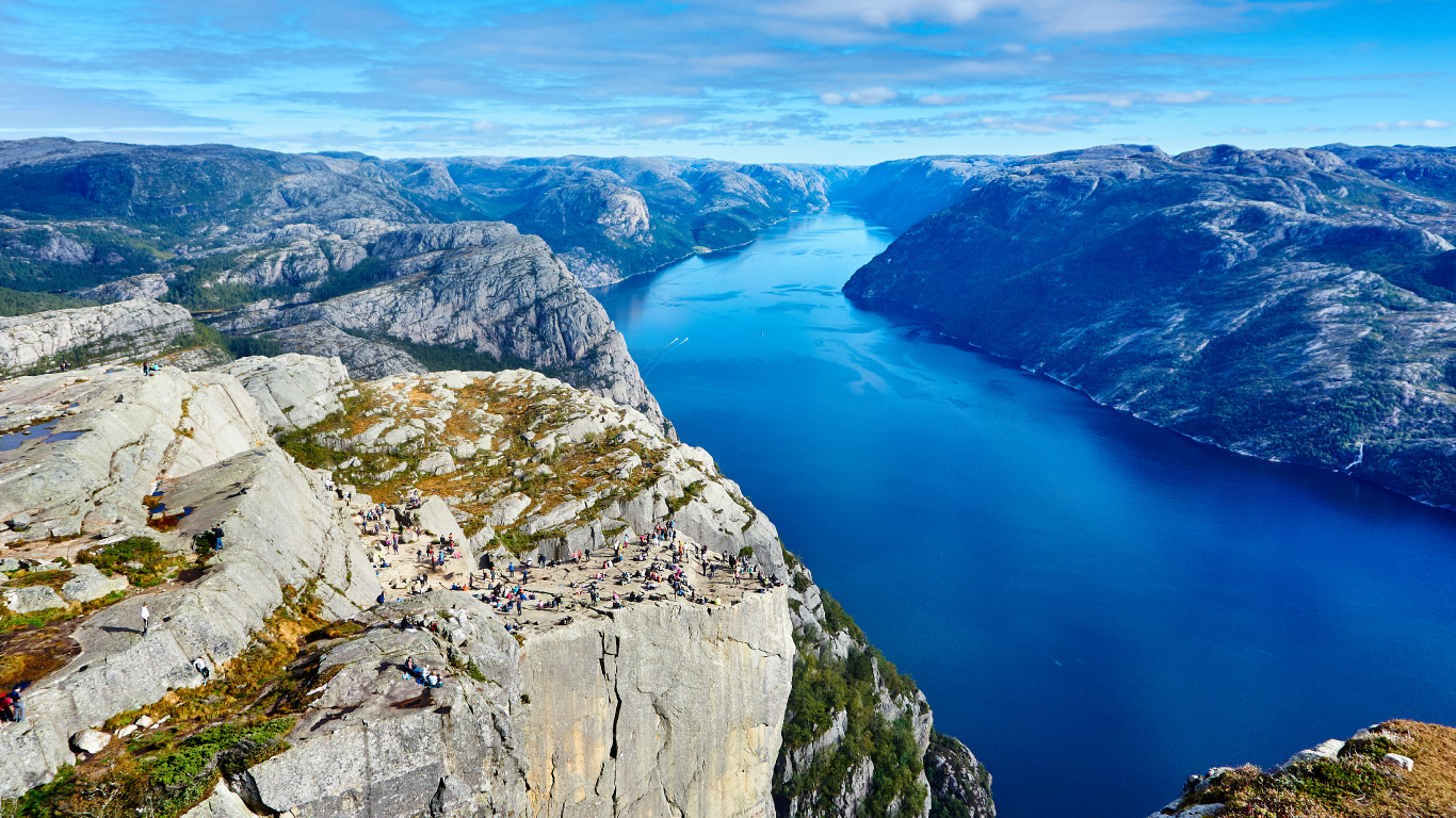 Blue Lake Between Gray Rocky Mountains Under Blue and White Sunny Cloudy Sky During Daytime. Wallpaper in 1366x768 Resolution