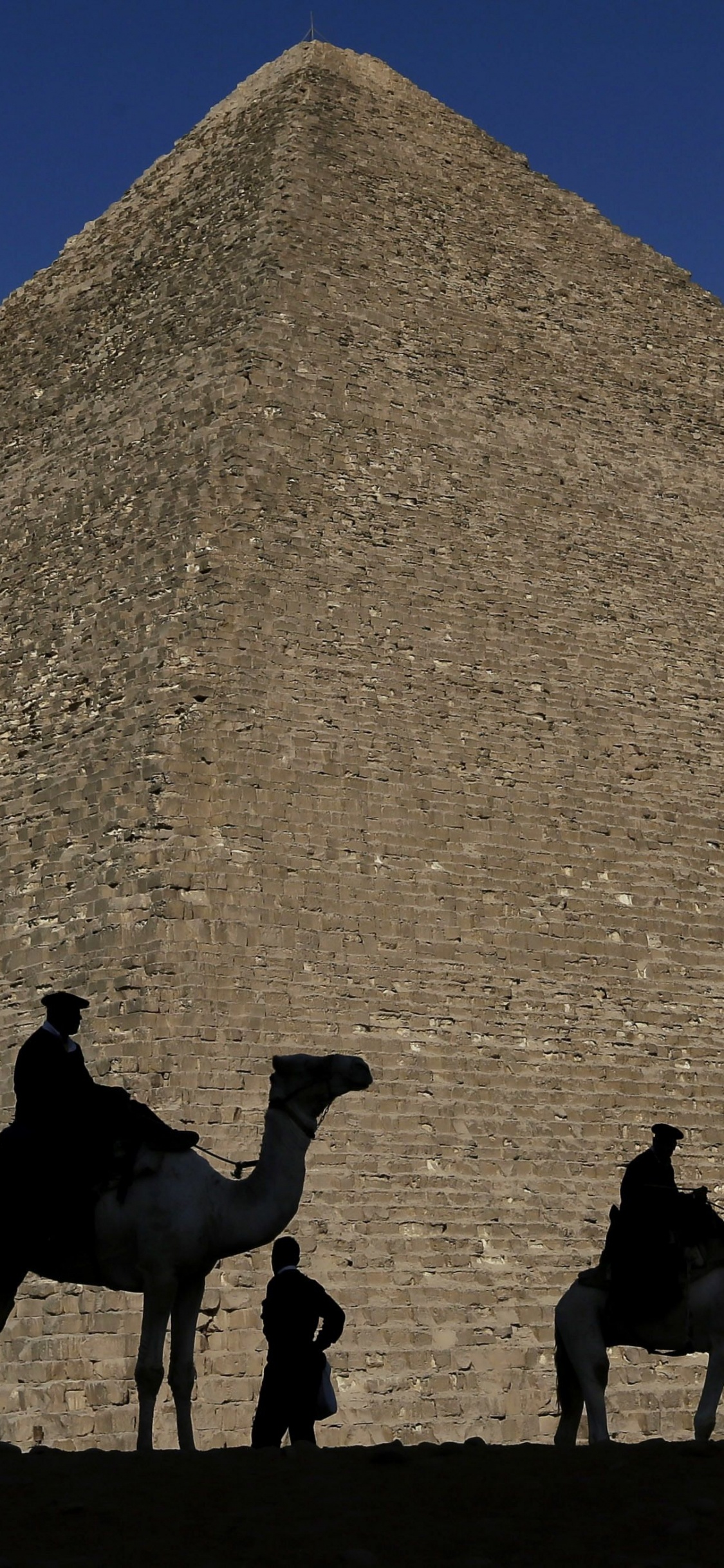 Group of People Riding Camels on Brown Sand Near Pyramid Under Blue Sky During Daytime. Wallpaper in 1125x2436 Resolution