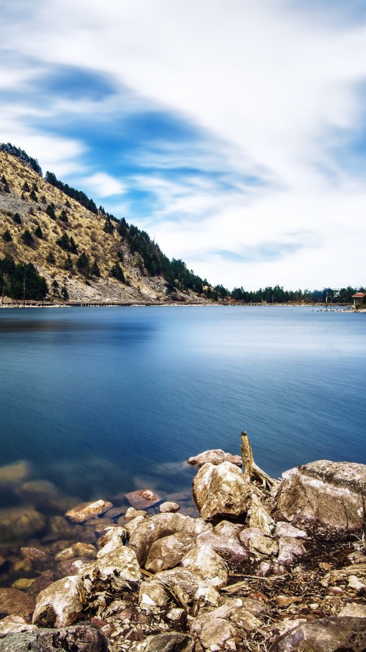 Person Sitting on Rock Near Body of Water During Daytime. Wallpaper in 750x1334 Resolution
