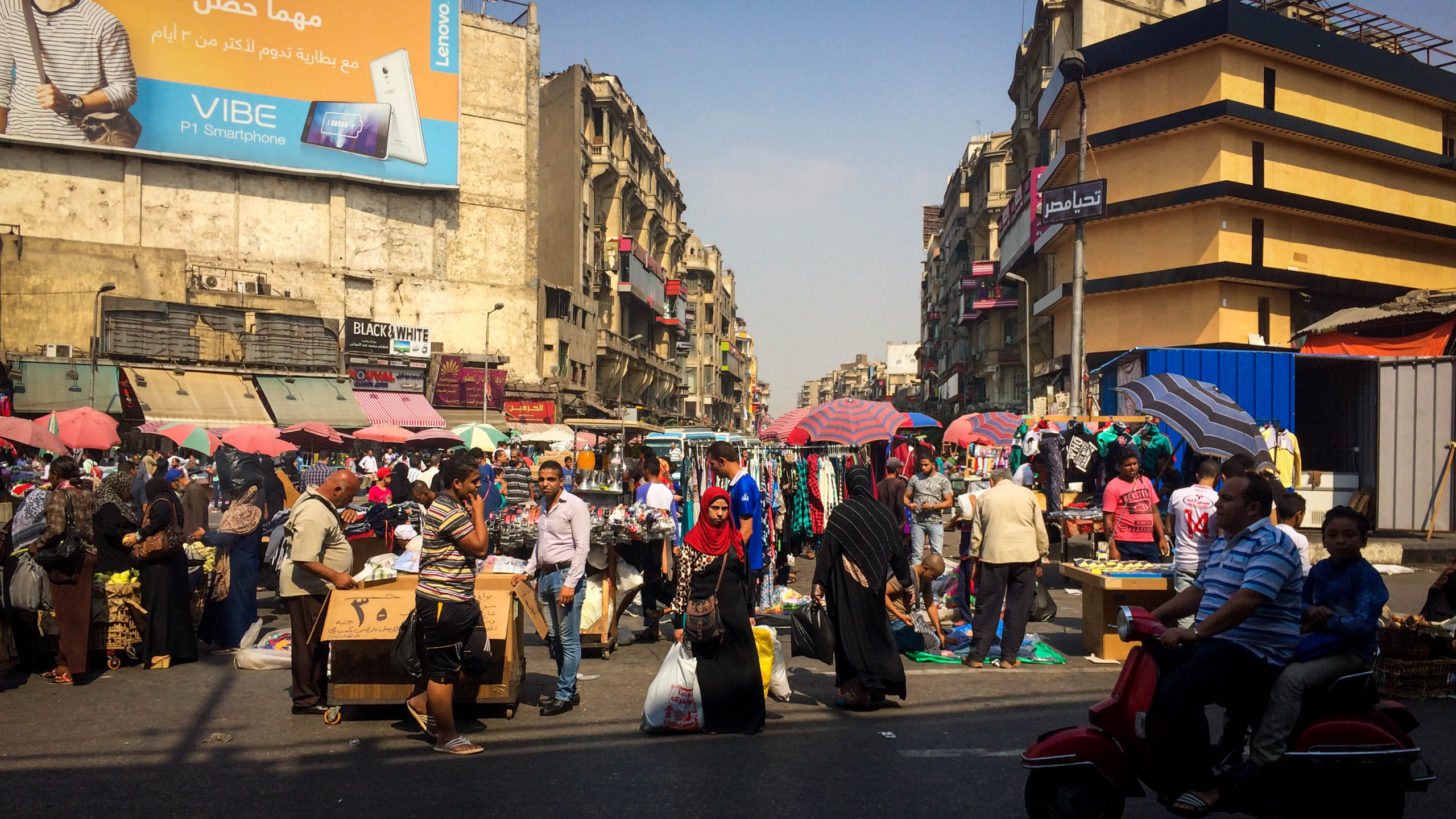 Personas en Una Calle Con Automóviles Estacionados a un Lado Durante el Día.. Wallpaper in 2560x1440 Resolution