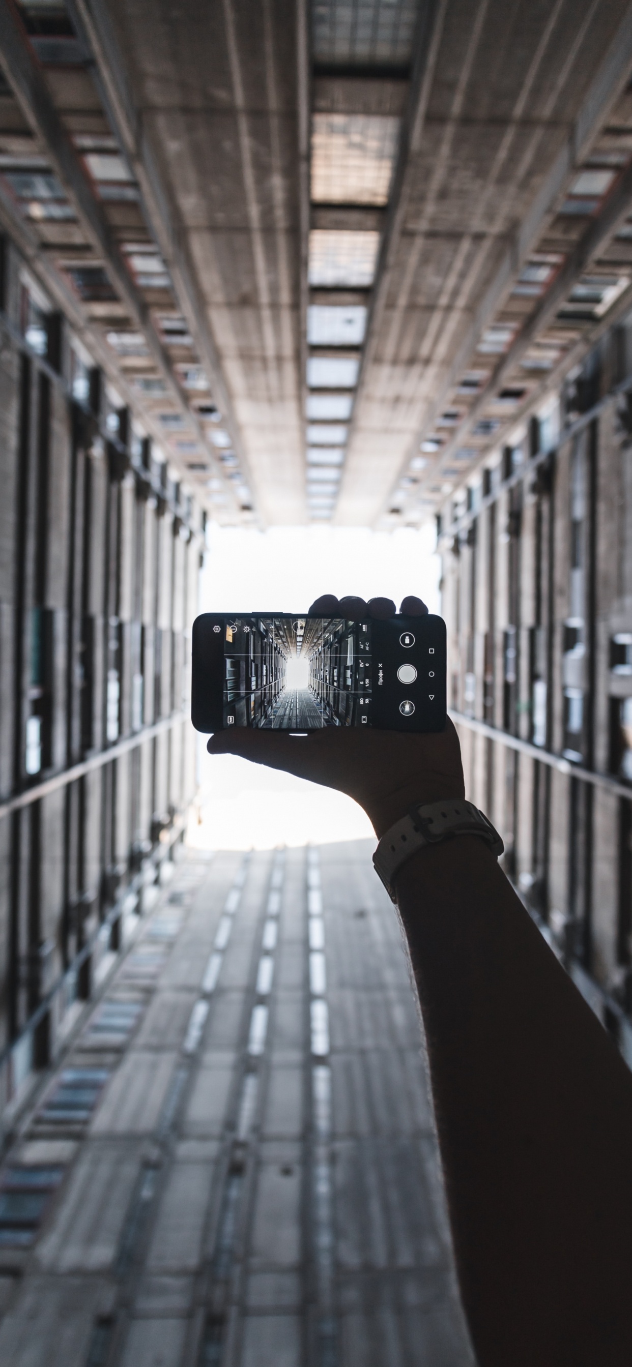 Person Holding Black Camera in Between of Building During Daytime. Wallpaper in 1242x2688 Resolution