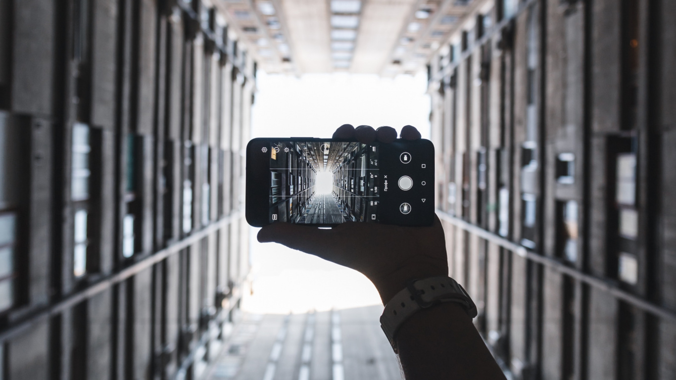 Person Holding Black Camera in Between of Building During Daytime. Wallpaper in 1366x768 Resolution