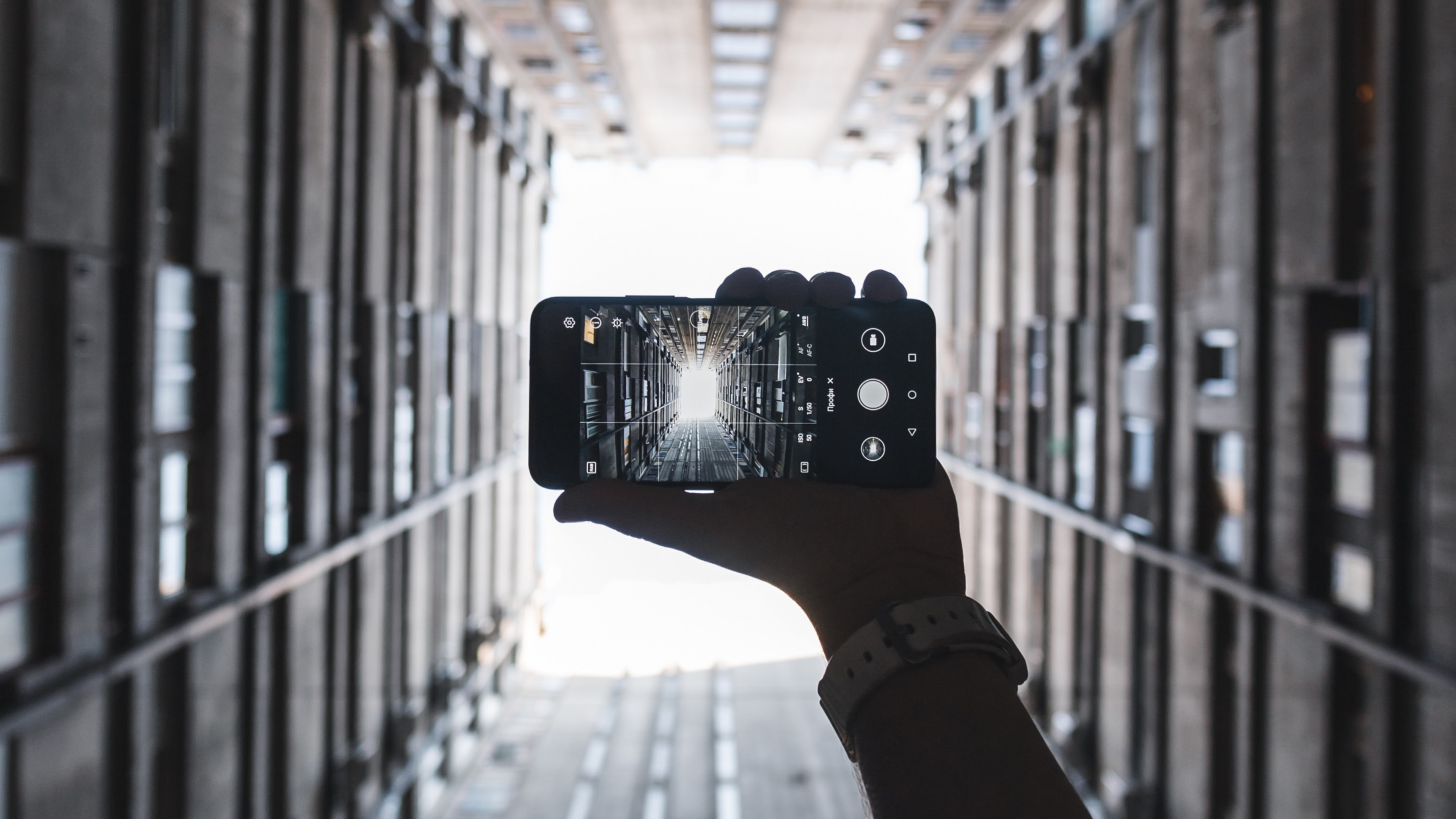 Person Holding Black Camera in Between of Building During Daytime. Wallpaper in 3840x2160 Resolution