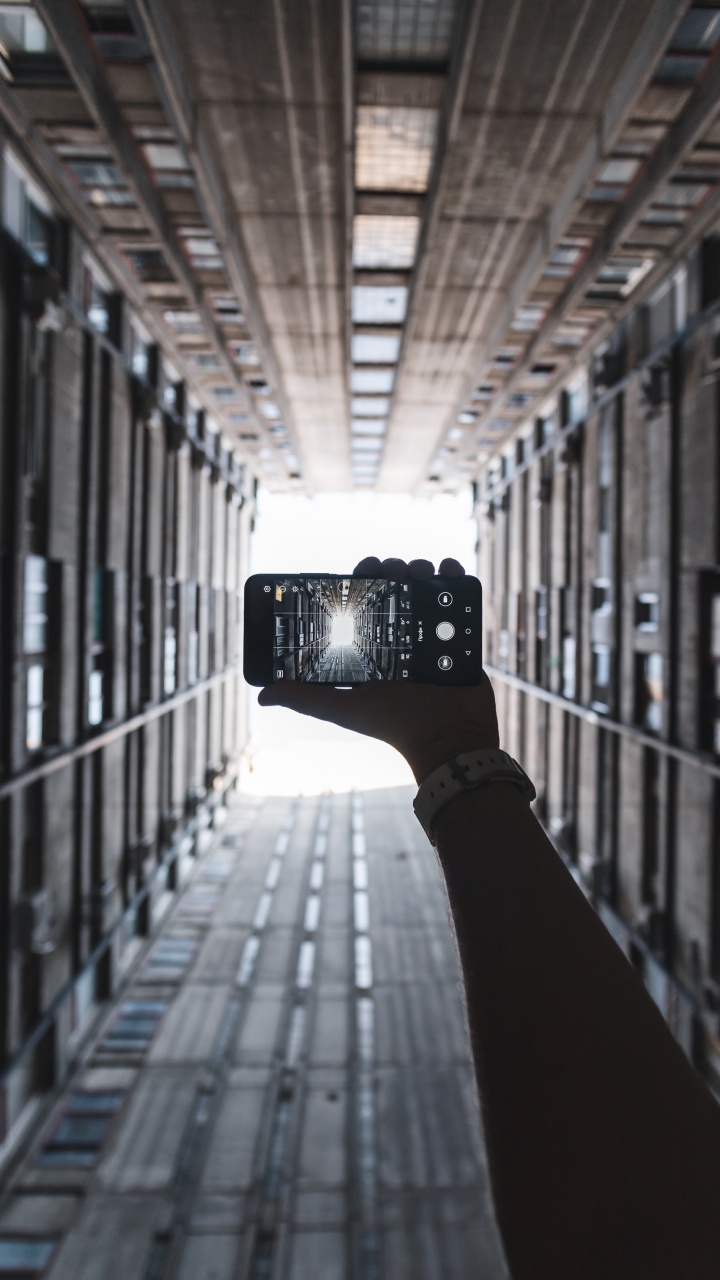 Person Holding Black Camera in Between of Building During Daytime. Wallpaper in 720x1280 Resolution