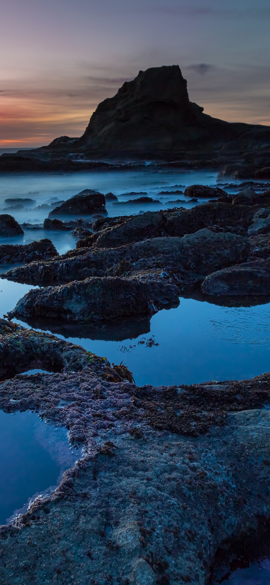 Rocky Shore Under Cloudy Sky During Daytime. Wallpaper in 1125x2436 Resolution