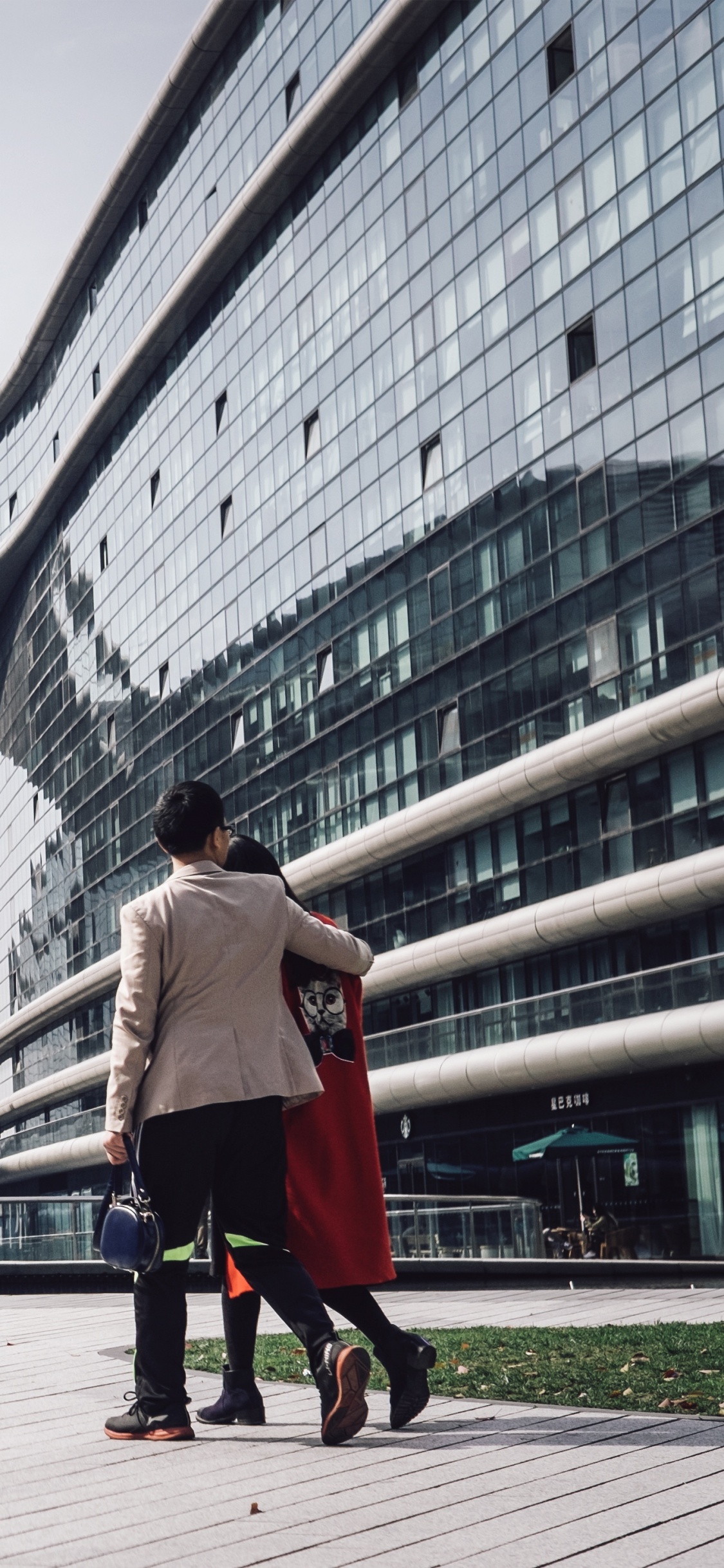 Woman in White Long Sleeve Shirt and Black Pants Walking on Sidewalk Near Glass Building During. Wallpaper in 1125x2436 Resolution