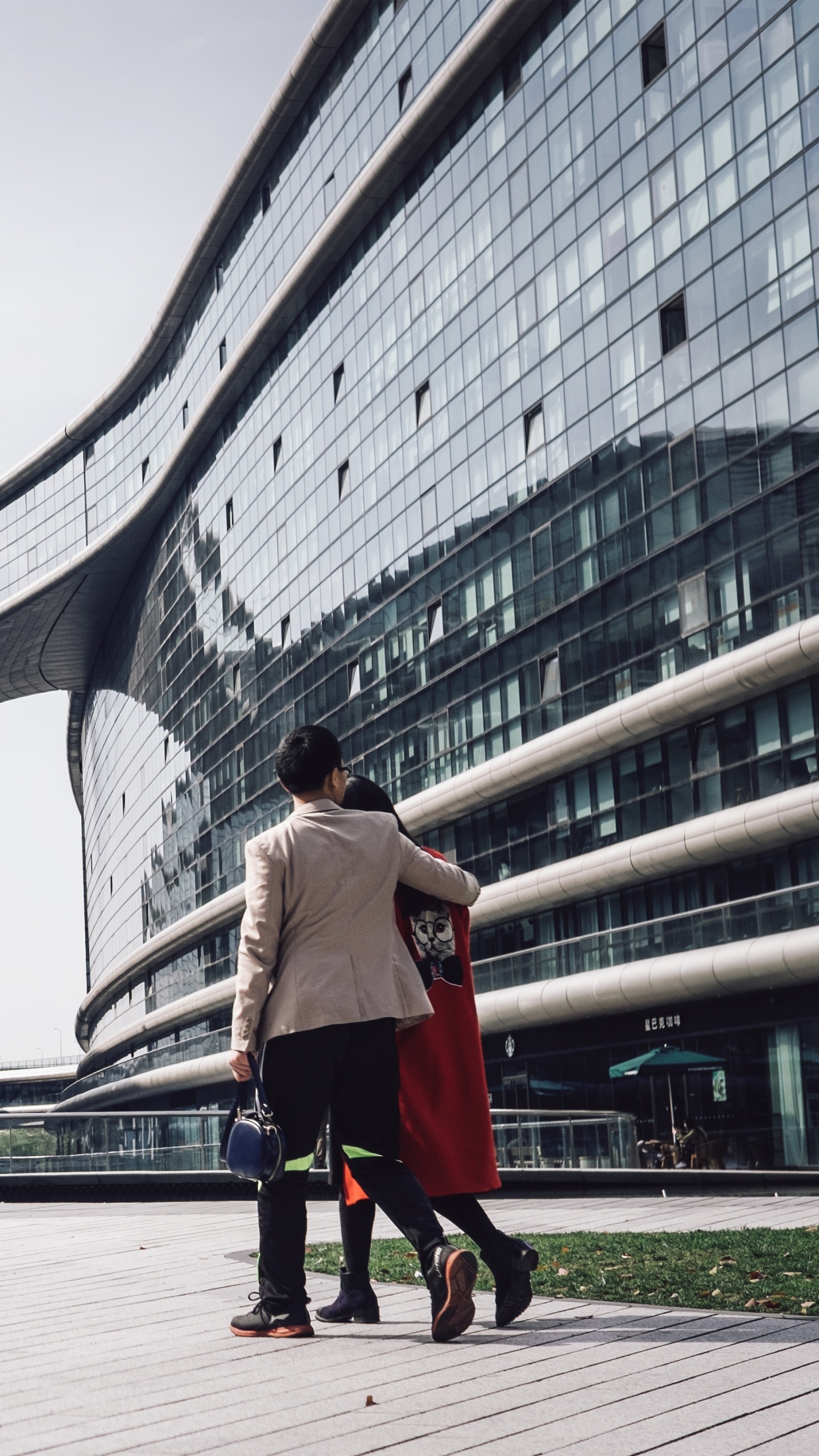 Woman in White Long Sleeve Shirt and Black Pants Walking on Sidewalk Near Glass Building During. Wallpaper in 1440x2560 Resolution