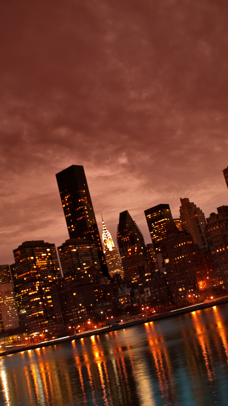 Skyline Der Stadt Über Gewässer Während Der Nacht. Wallpaper in 750x1334 Resolution