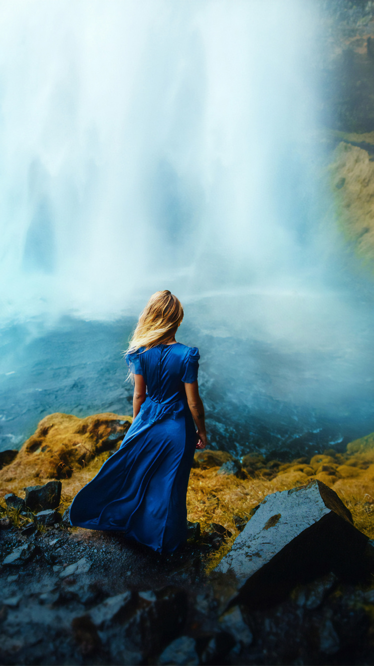Mujer en Chaqueta Azul Sentada Sobre Una Roca Cerca de Cascadas Durante el Día. Wallpaper in 750x1334 Resolution