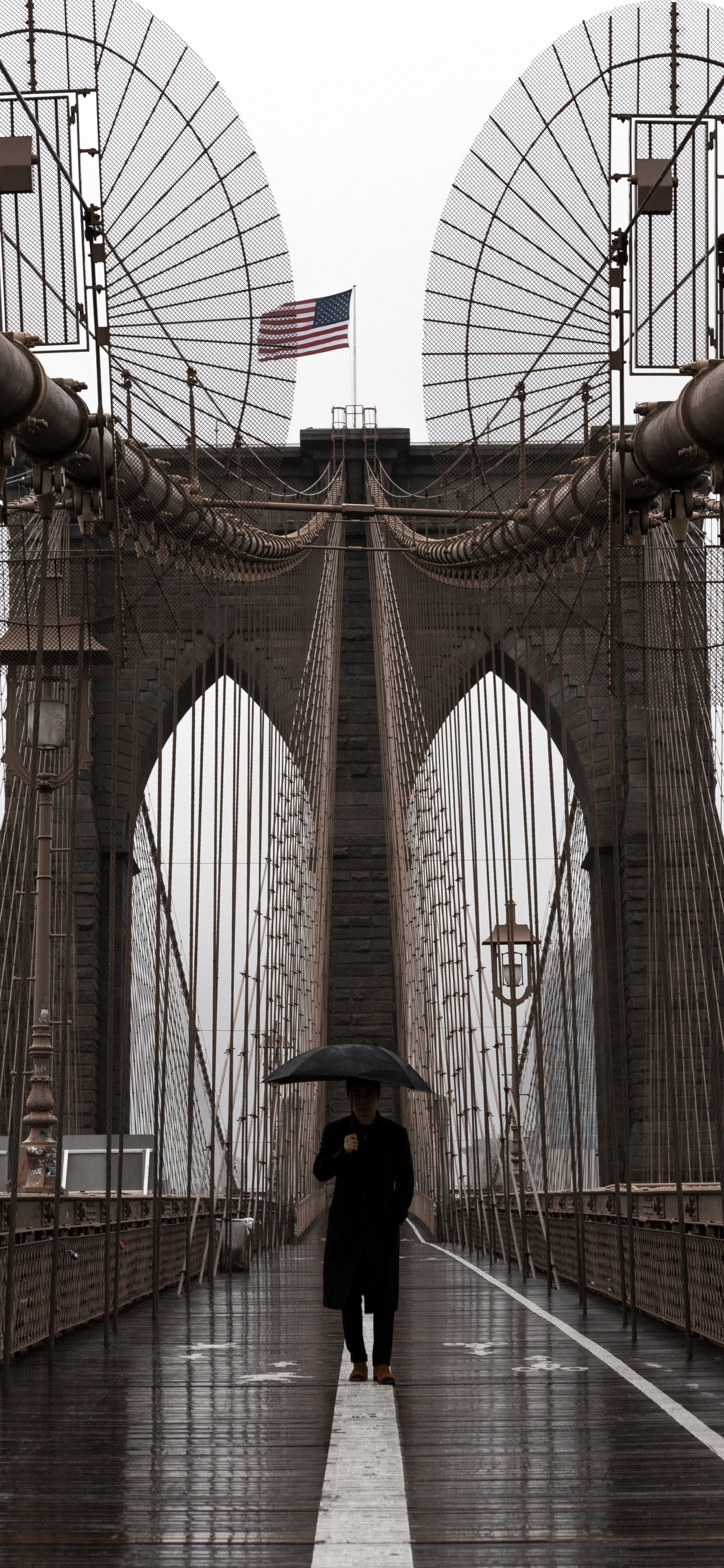 Frau in Schwarzer Jacke Und Schwarzer Hose, Die Tagsüber Auf Der Brücke Läuft. Wallpaper in 1242x2688 Resolution