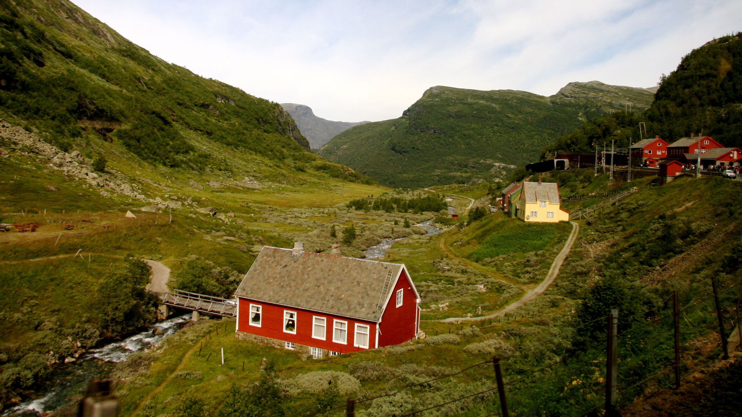 Rotes Und Weißes Haus Auf Grüner Wiese in Der Nähe Von Grünen Bergen Unter Weißen Wolken Und Blau. Wallpaper in 2560x1440 Resolution