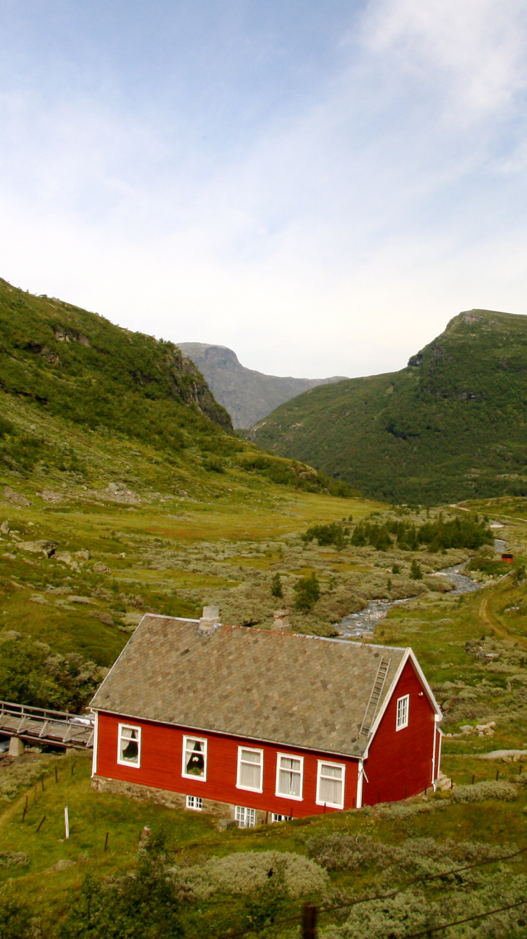 Red and White House on Green Grass Field Near Green Mountains Under White Clouds and Blue. Wallpaper in 750x1334 Resolution